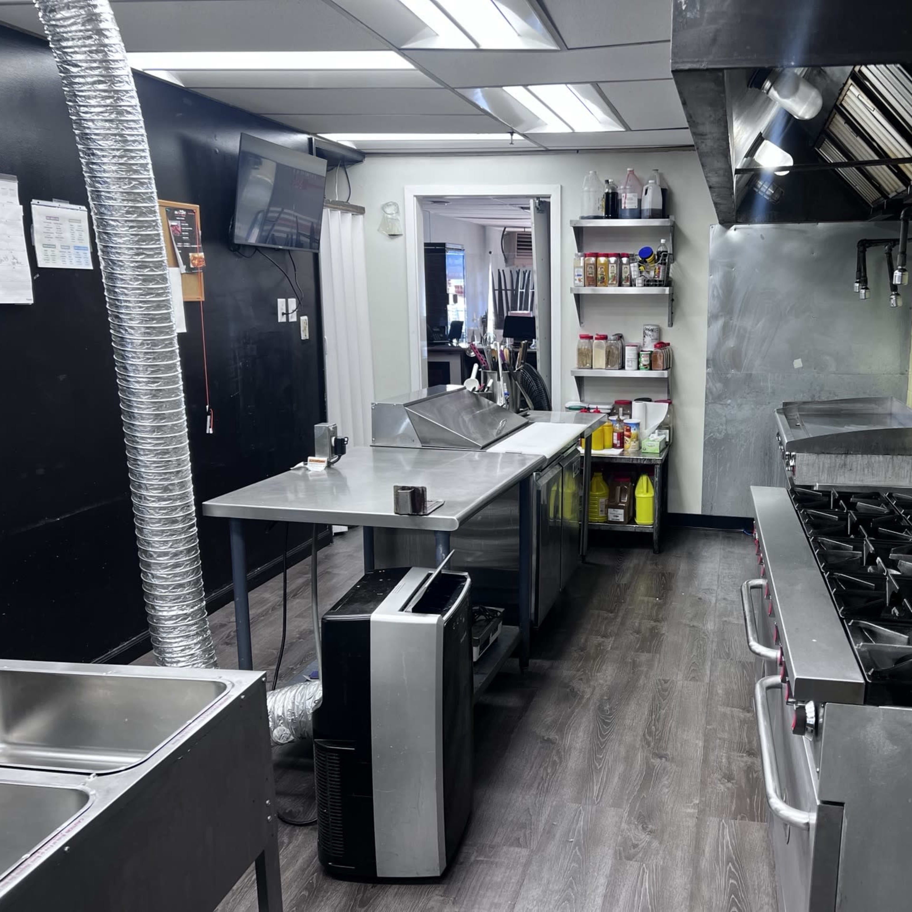 A commercial kitchen with stainless steel appliances, a central preparation table, and shelves stocked with various food items and kitchen supplies.