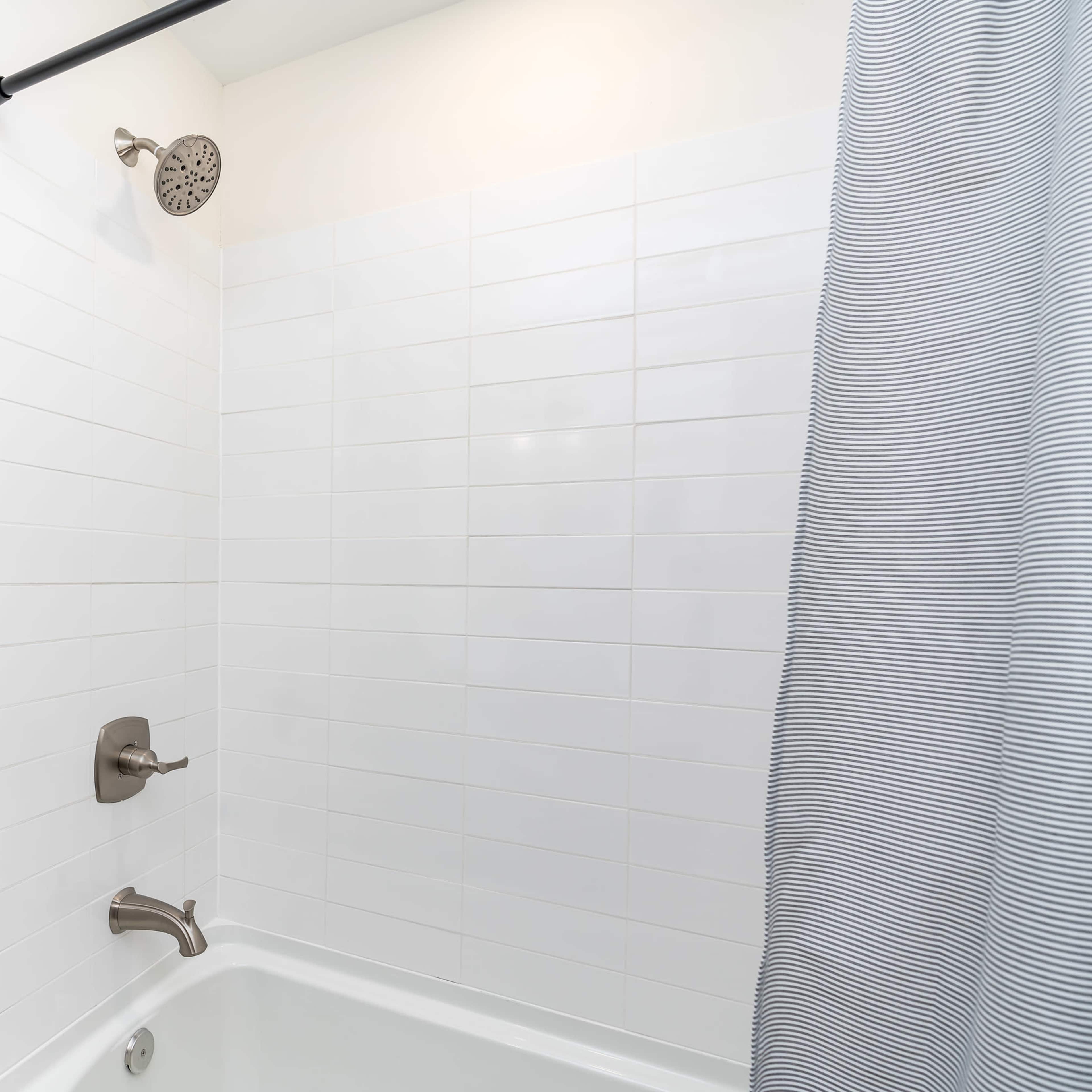 A clean bathroom shower area with a white tiled wall, a showerhead, and a striped curtain.