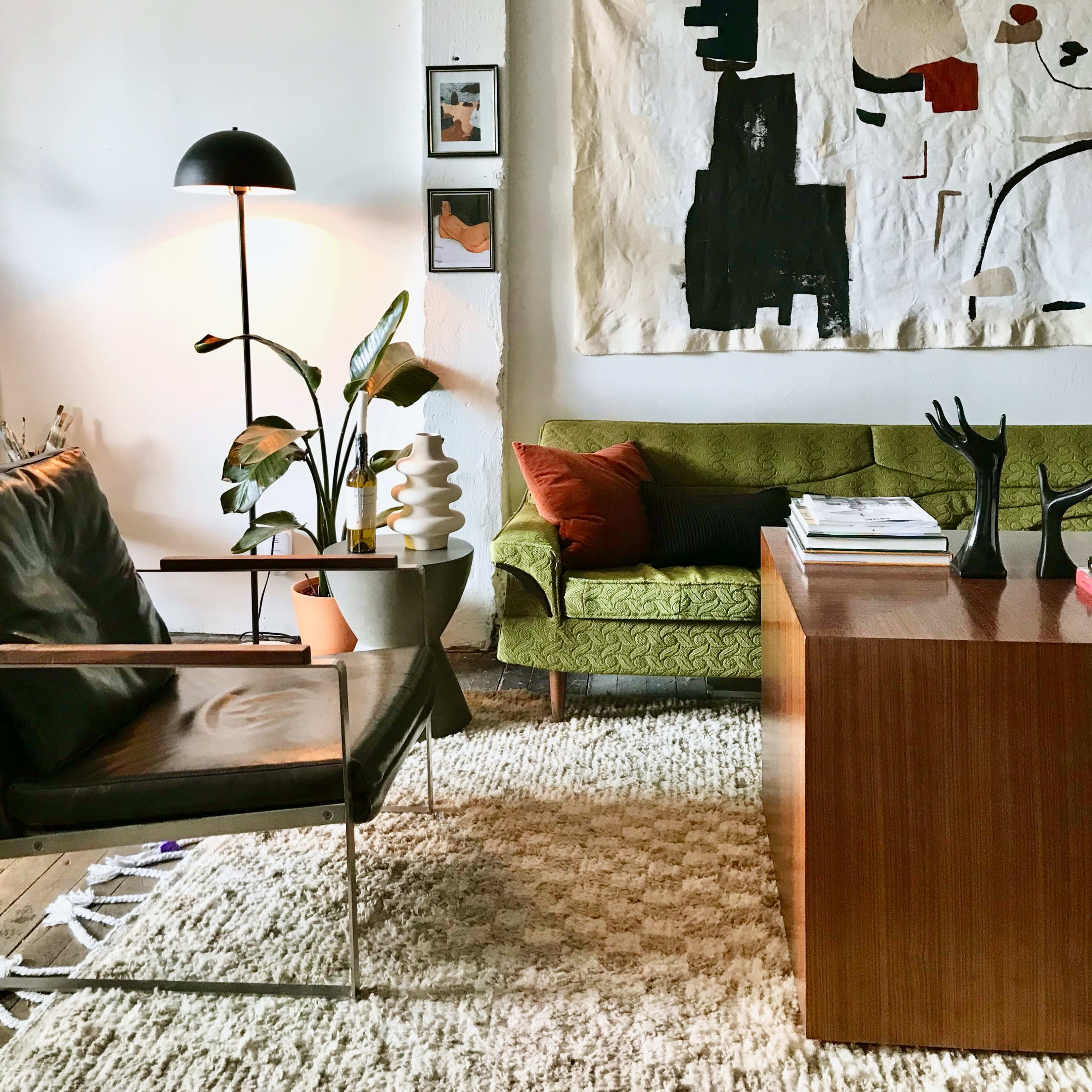 A modern living room with a green couch, a wooden coffee table, a floor lamp, and abstract wall art.