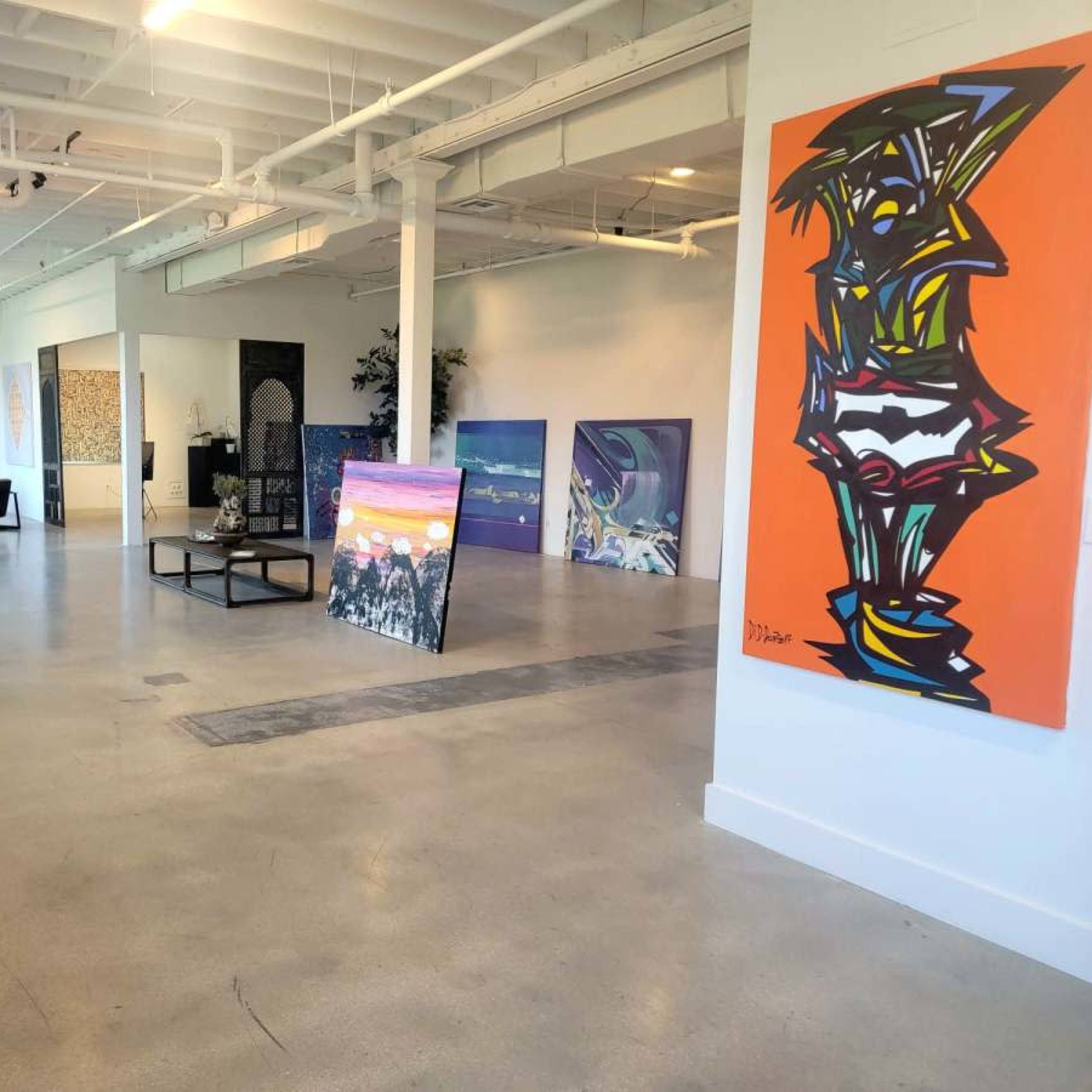 A spacious art gallery with various colorful artworks displayed on the walls and large canvases positioned in the center.