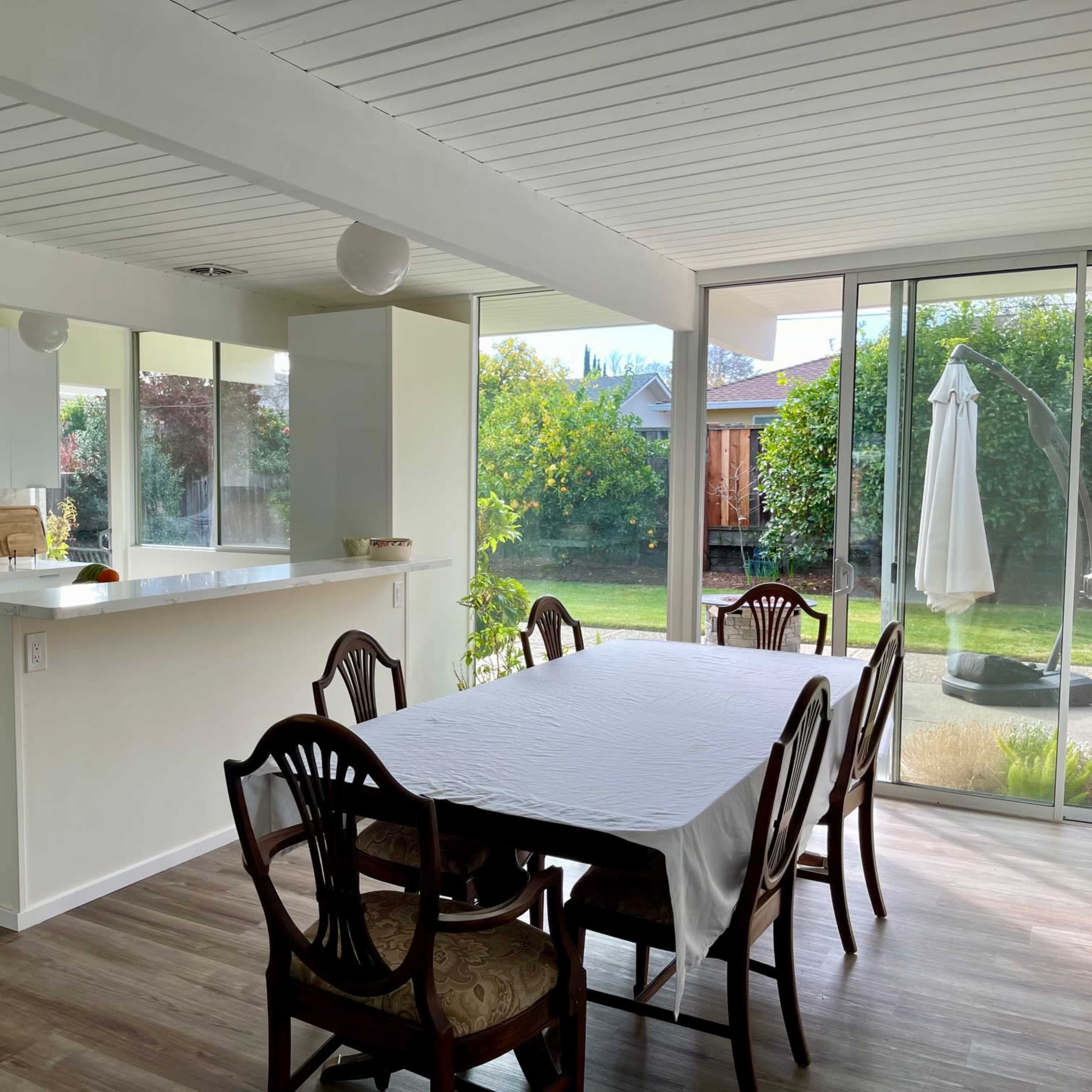 A modern kitchen and dining area with a table set for six and large windows overlooking a garden.