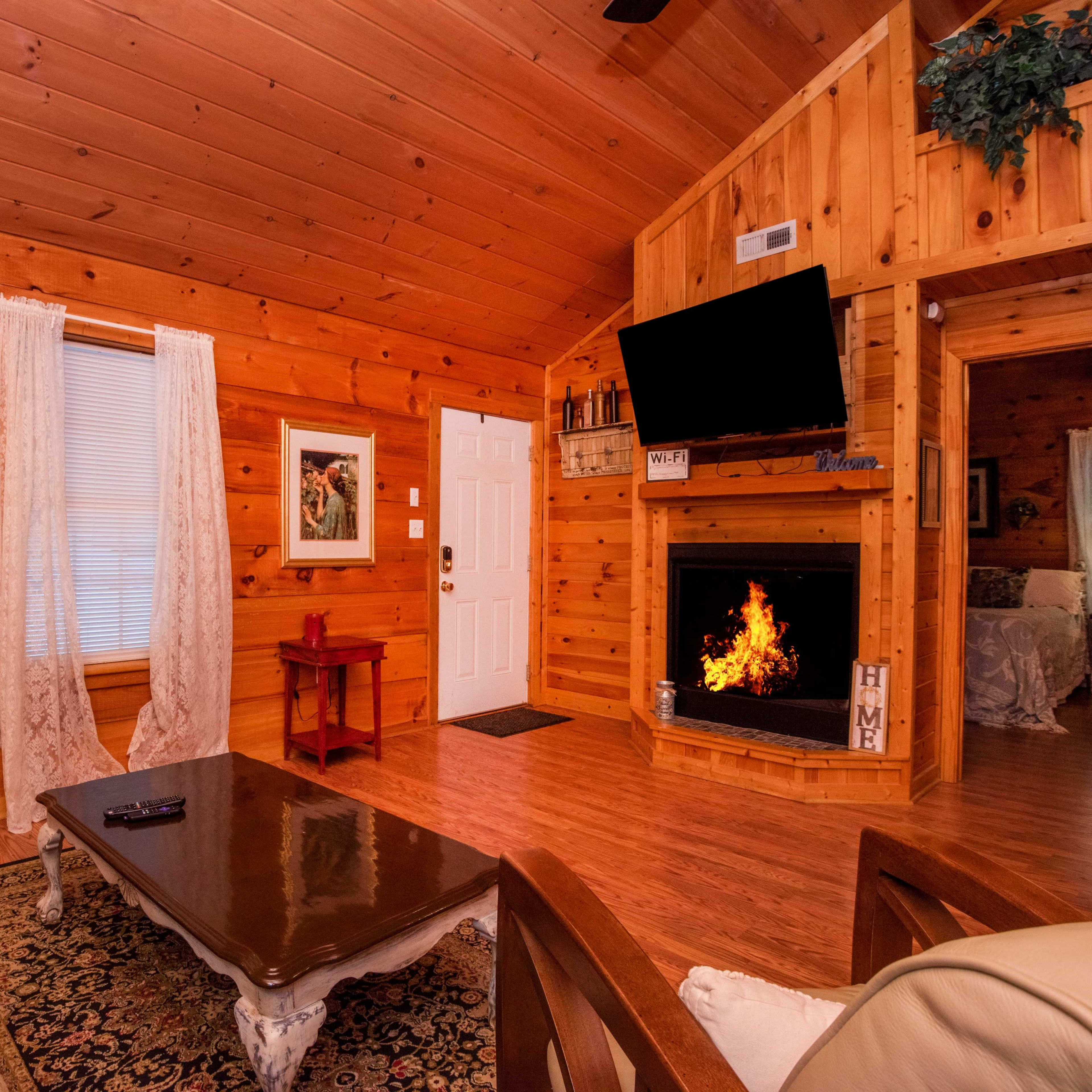 A rustic wooden living room with a sofa, a coffee table, and a fireplace with an artificial flame.