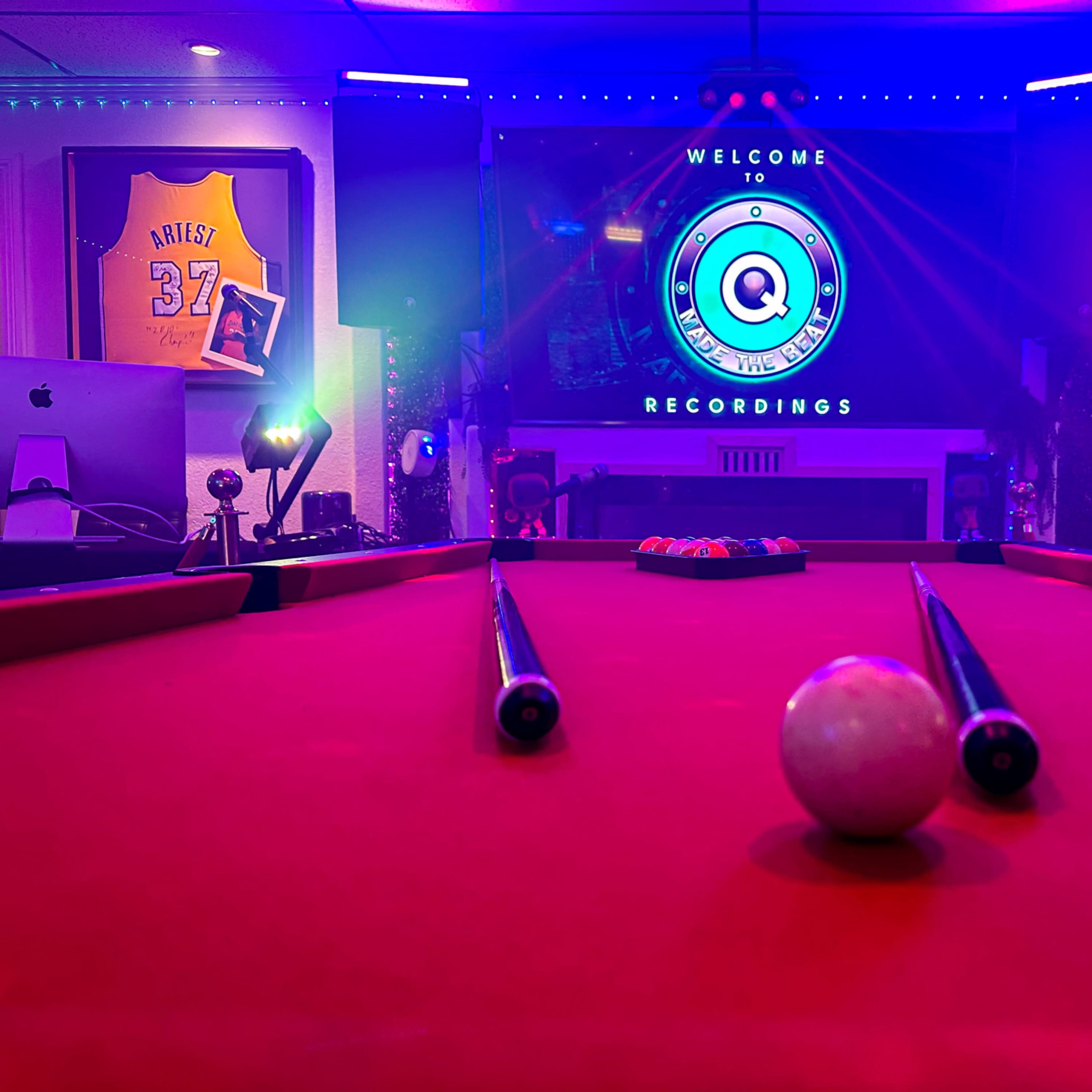 A pool table with a white ball in the foreground is centered in a room featuring colorful lighting and framed jerseys on the walls.