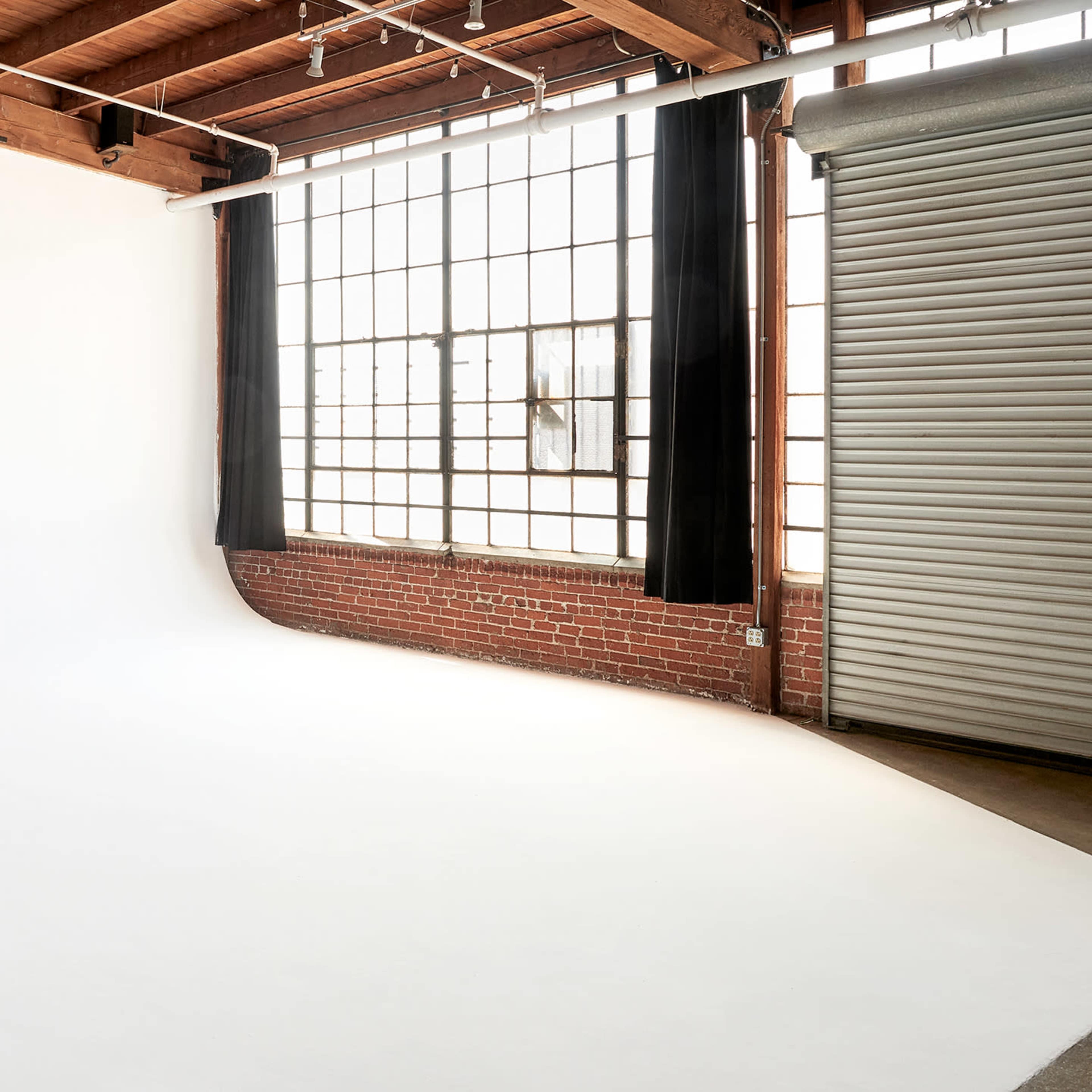 A spacious photography studio with a white backdrop, large windows, and a brick wall.