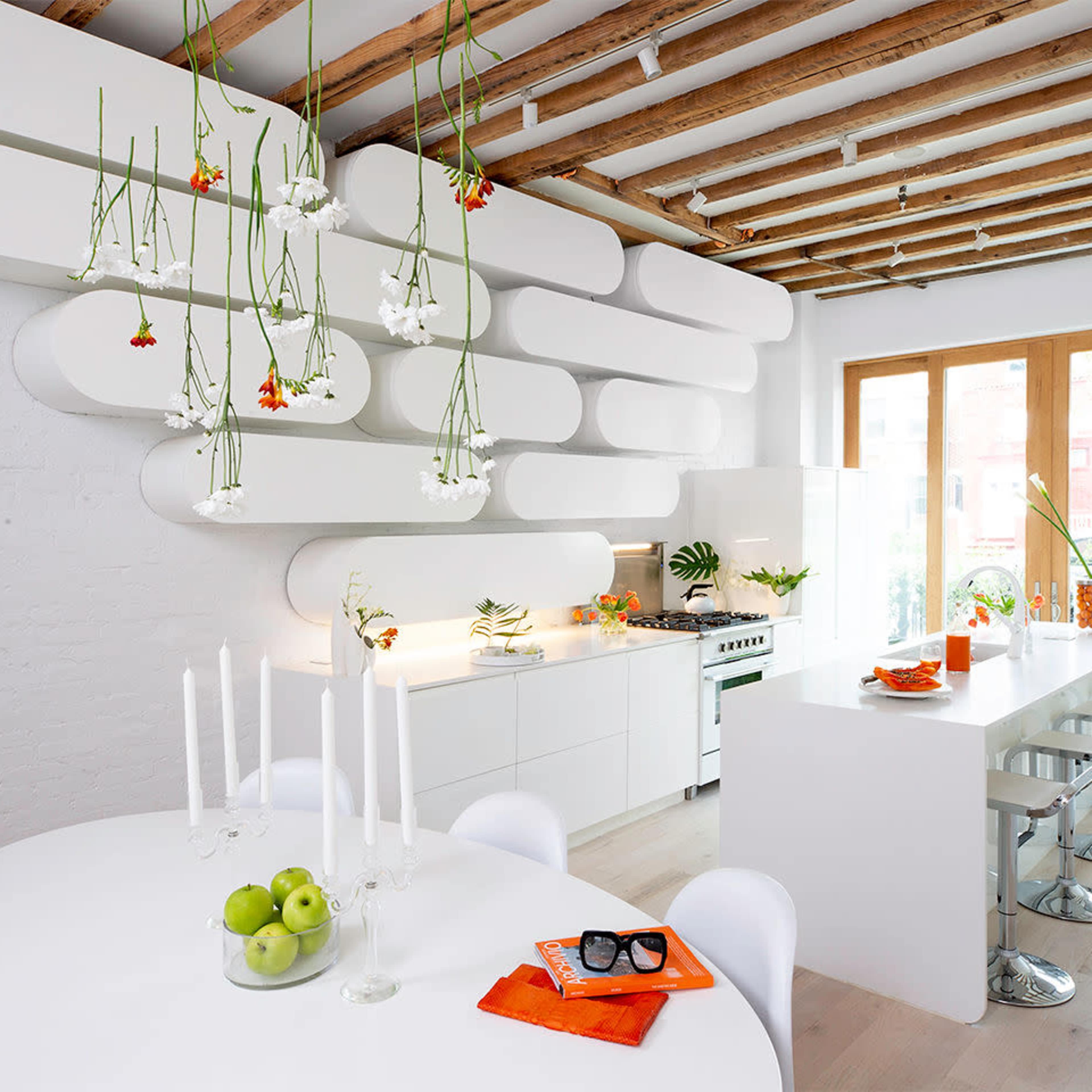 A modern kitchen features a minimalist design with a round dining table, white cabinetry, and floating shelves adorned with plants.