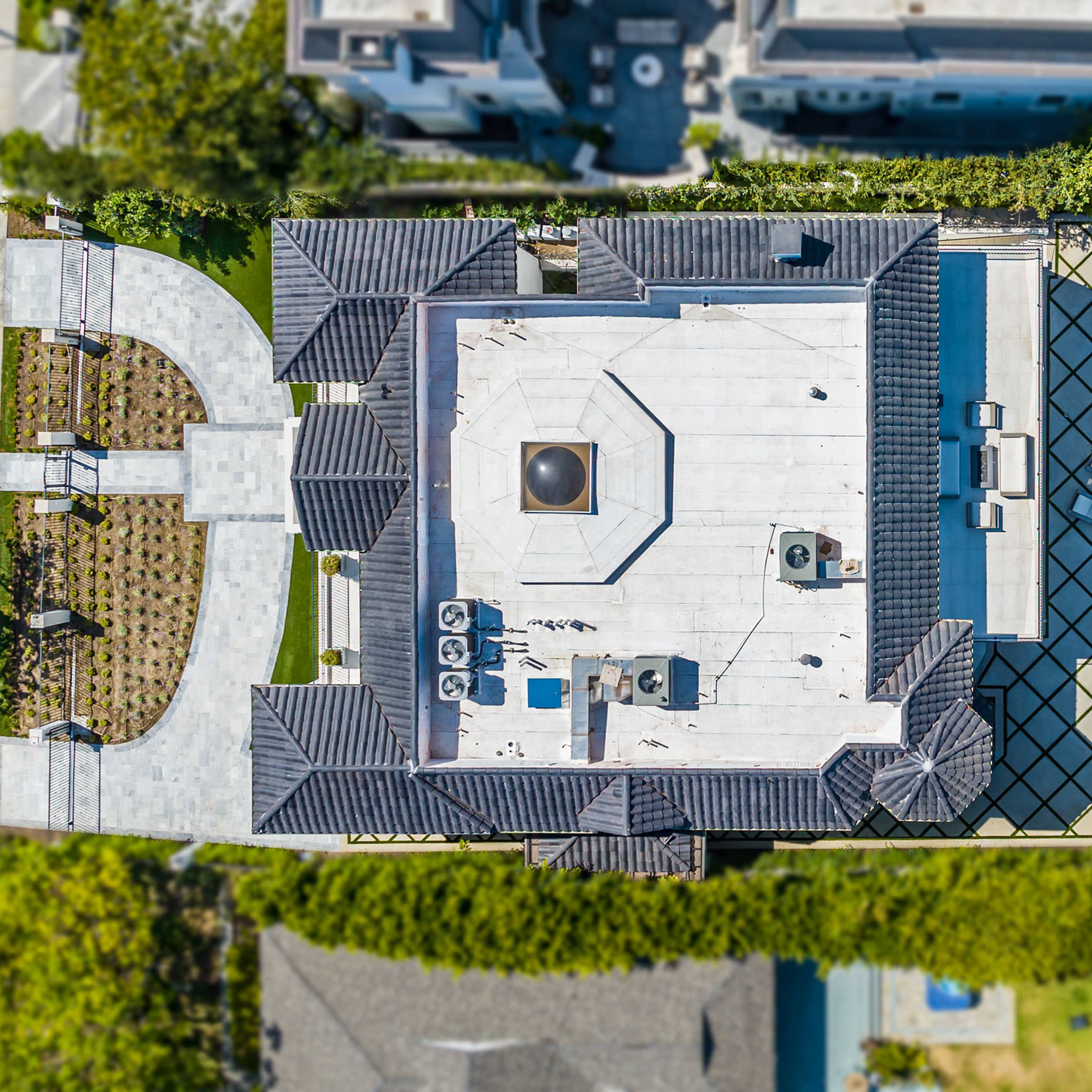 An aerial view of a large residential property featuring a flat-roofed house, a swimming pool, a tennis court, and landscaped areas.