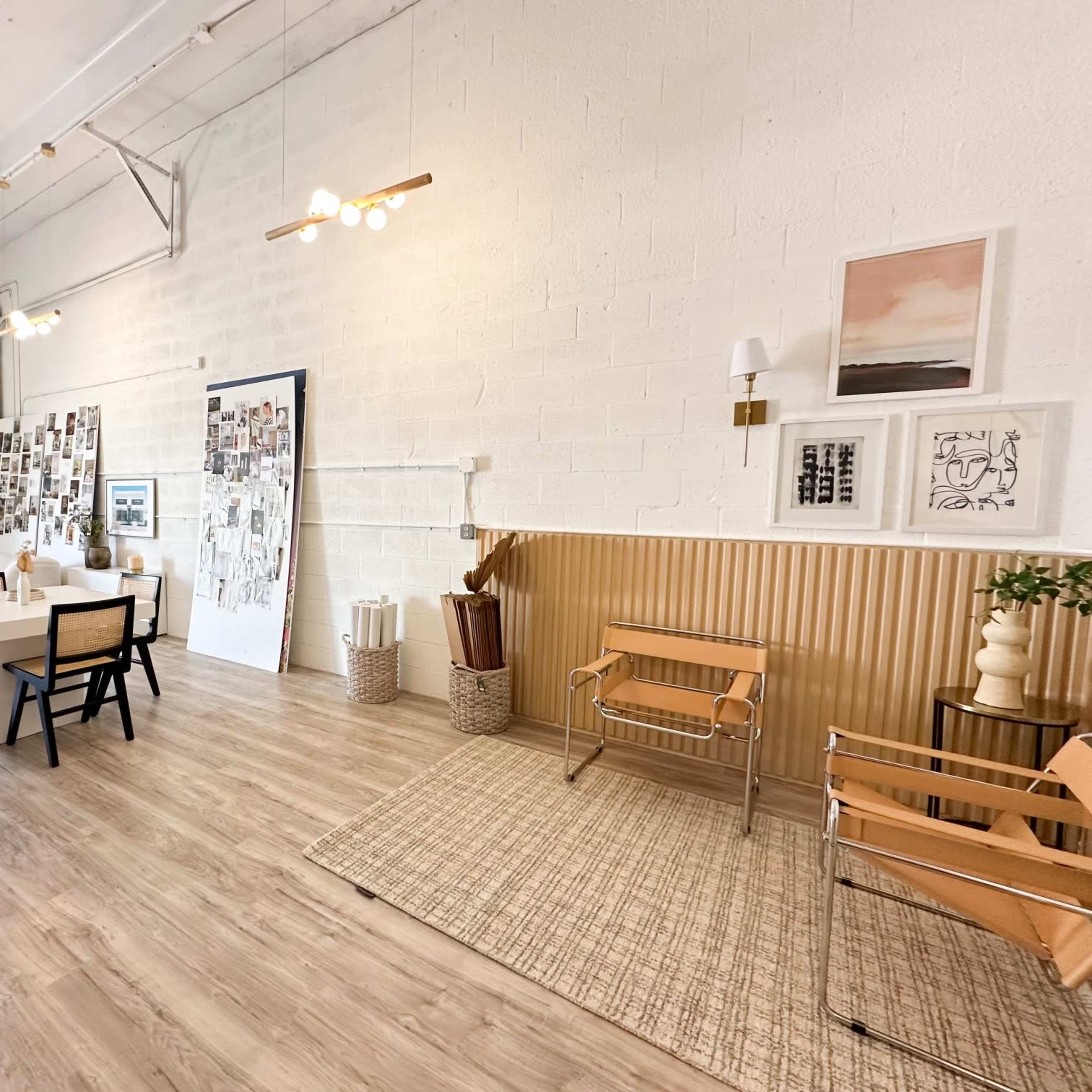 A spacious room with a large table and chairs, decorated with wall art and a gallery of photos, featuring light wood flooring and modern lighting fixtures.