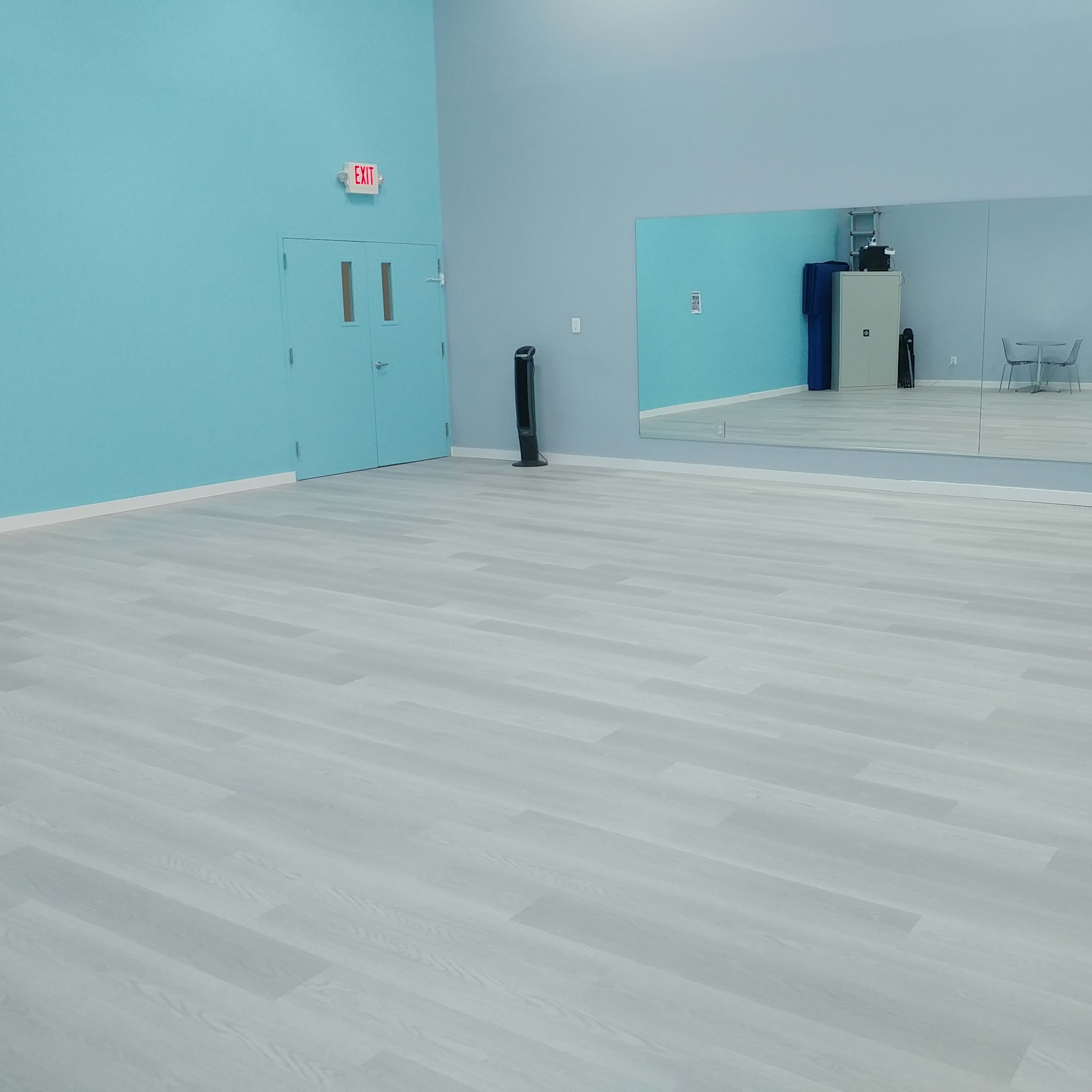 A spacious room with light gray flooring, light blue walls, a large mirror on one side, and a couch against the wall.