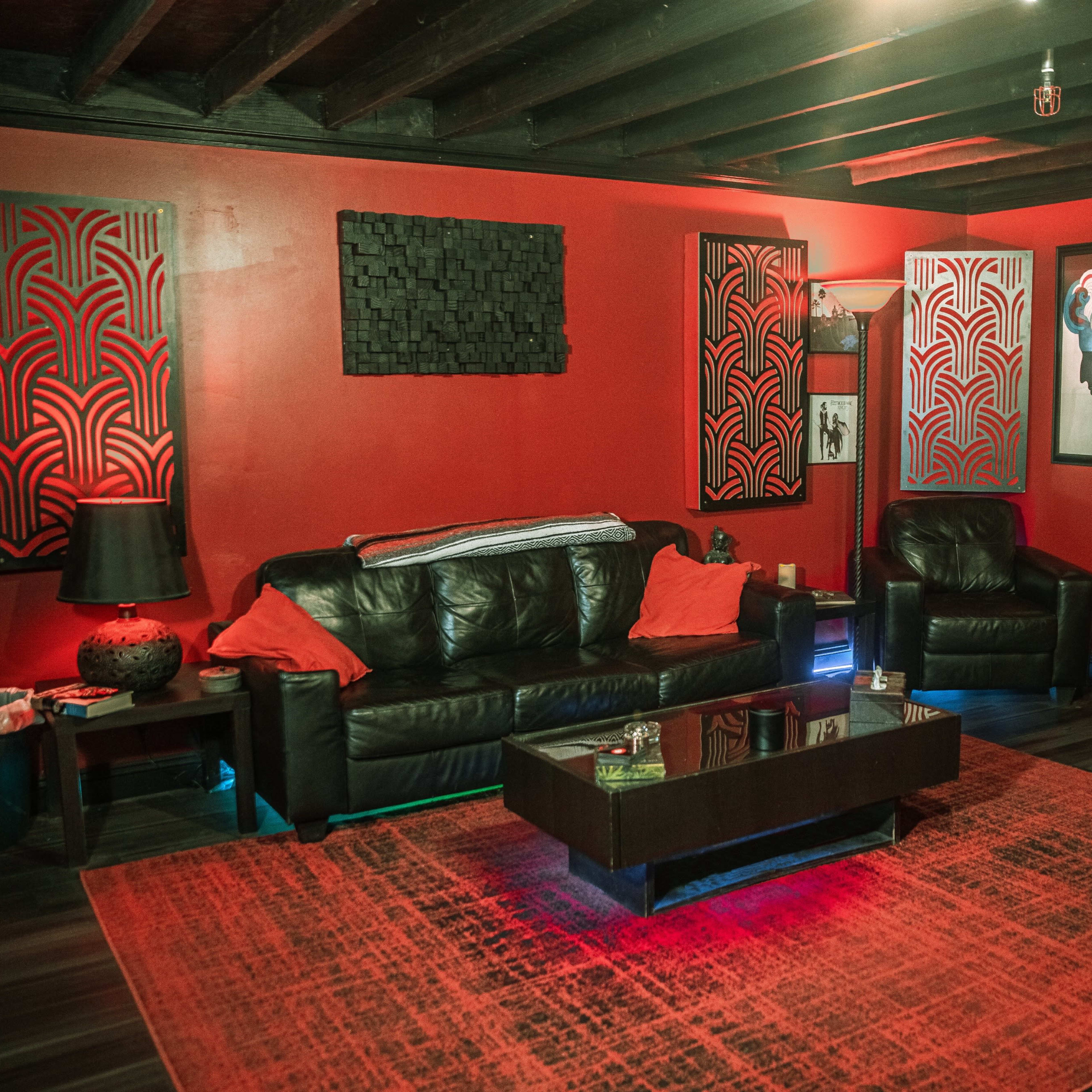 A modern living room with red walls, black leather furniture, and decorative artwork on the walls.