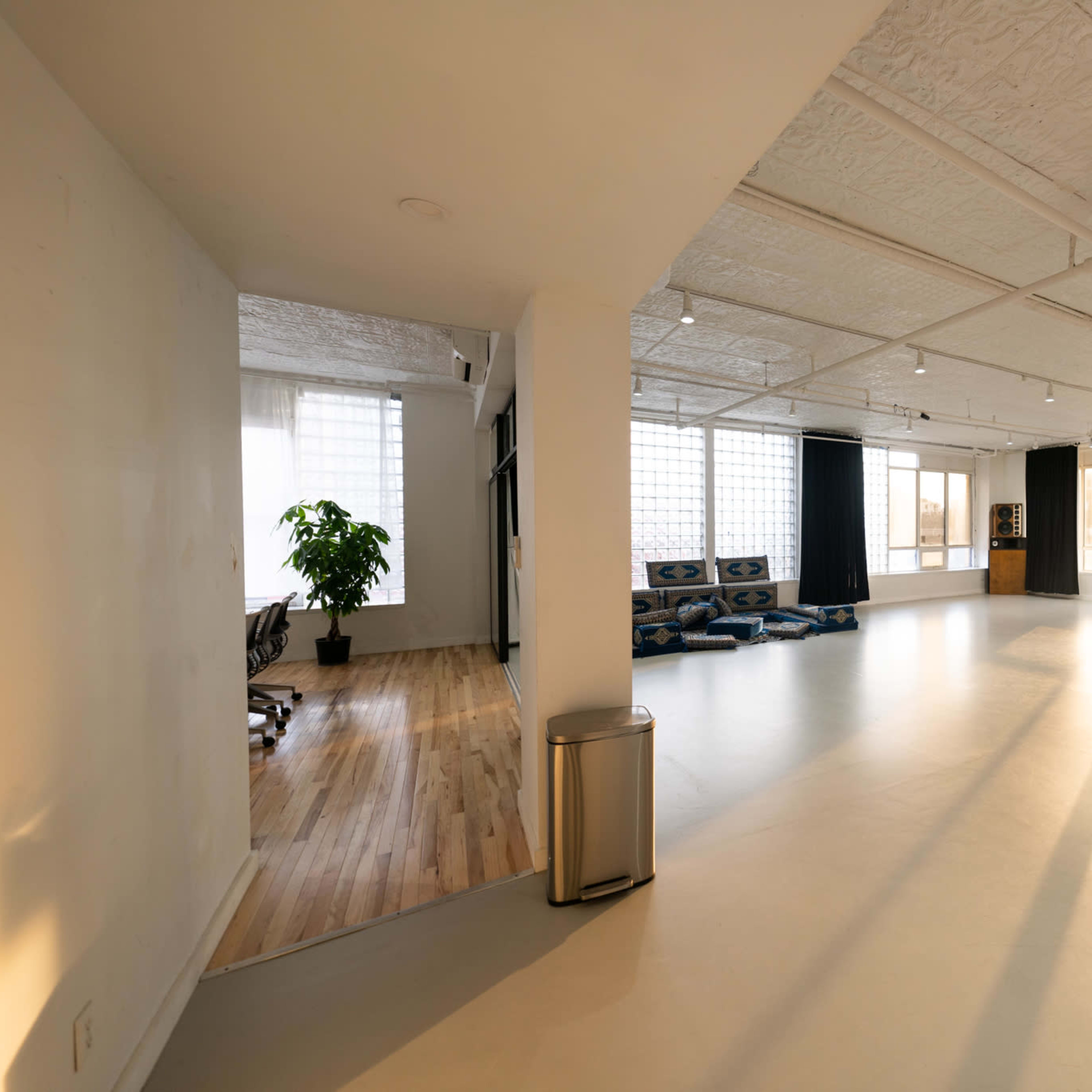 An open-concept workspace with large windows, minimalist decor, and a seating area featuring blue cushions.