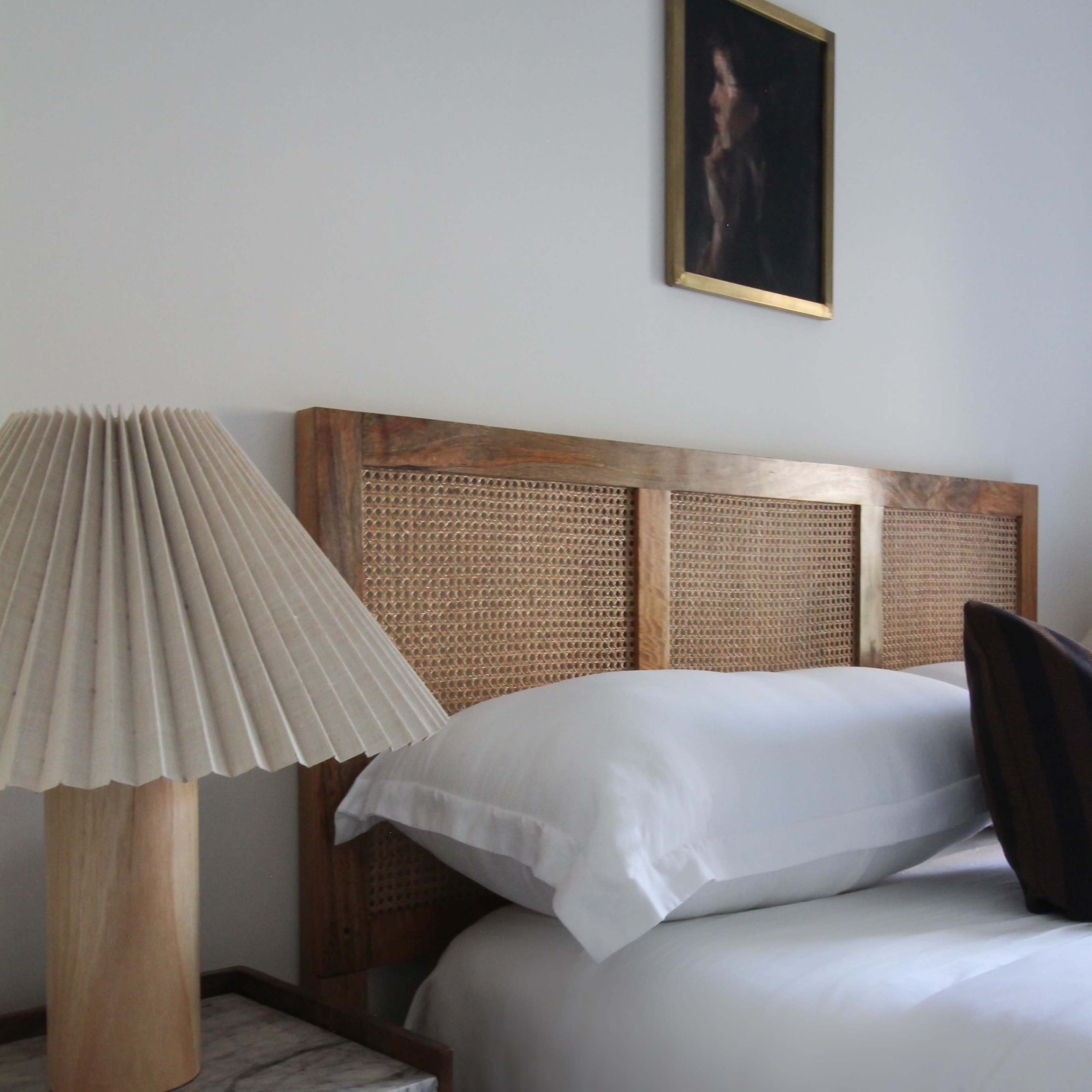 A bed with a wooden headboard and decorative lamp sits beside a nightstand in a softly lit bedroom.