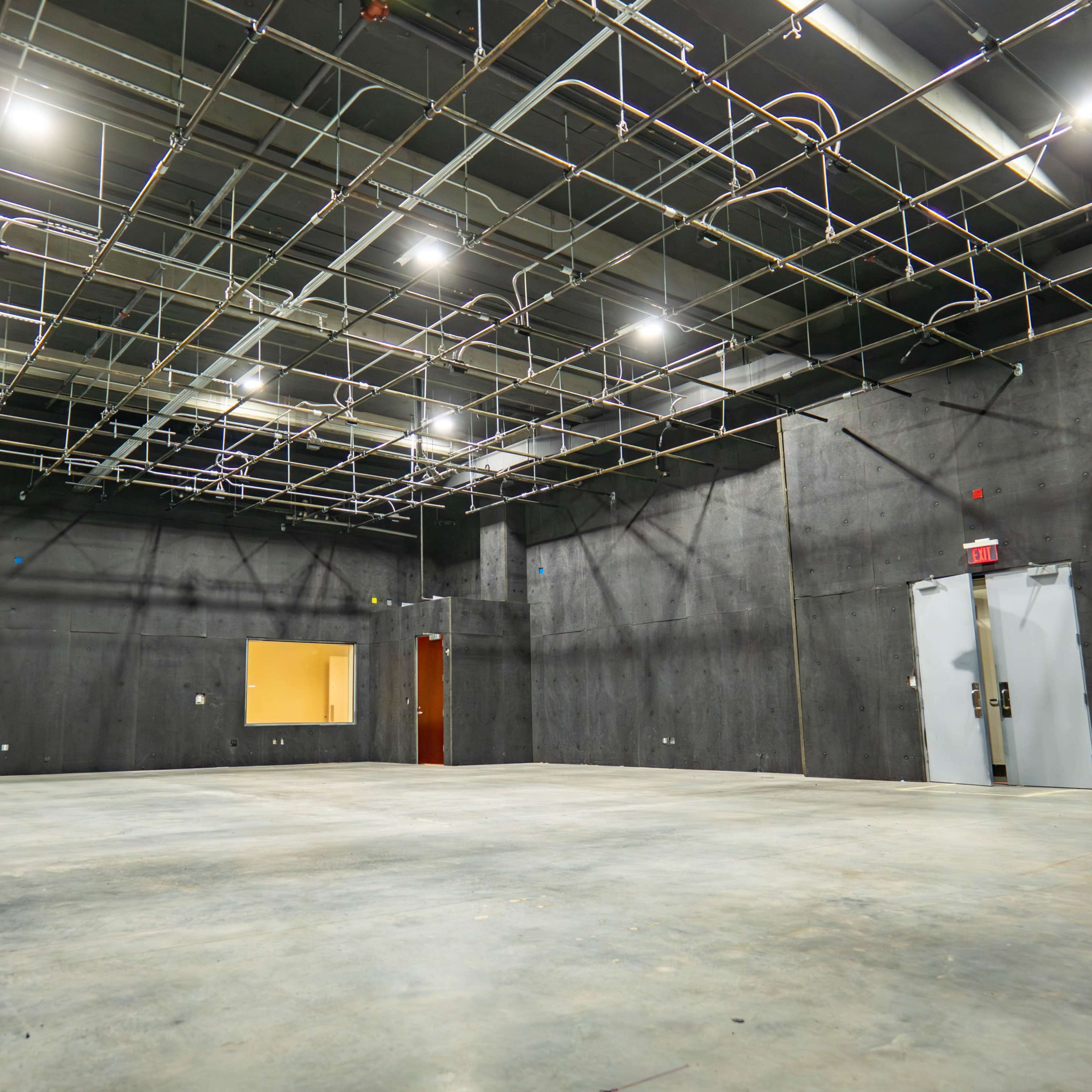 An empty industrial space features concrete walls, a bare concrete floor, and overhead lighting fixtures.