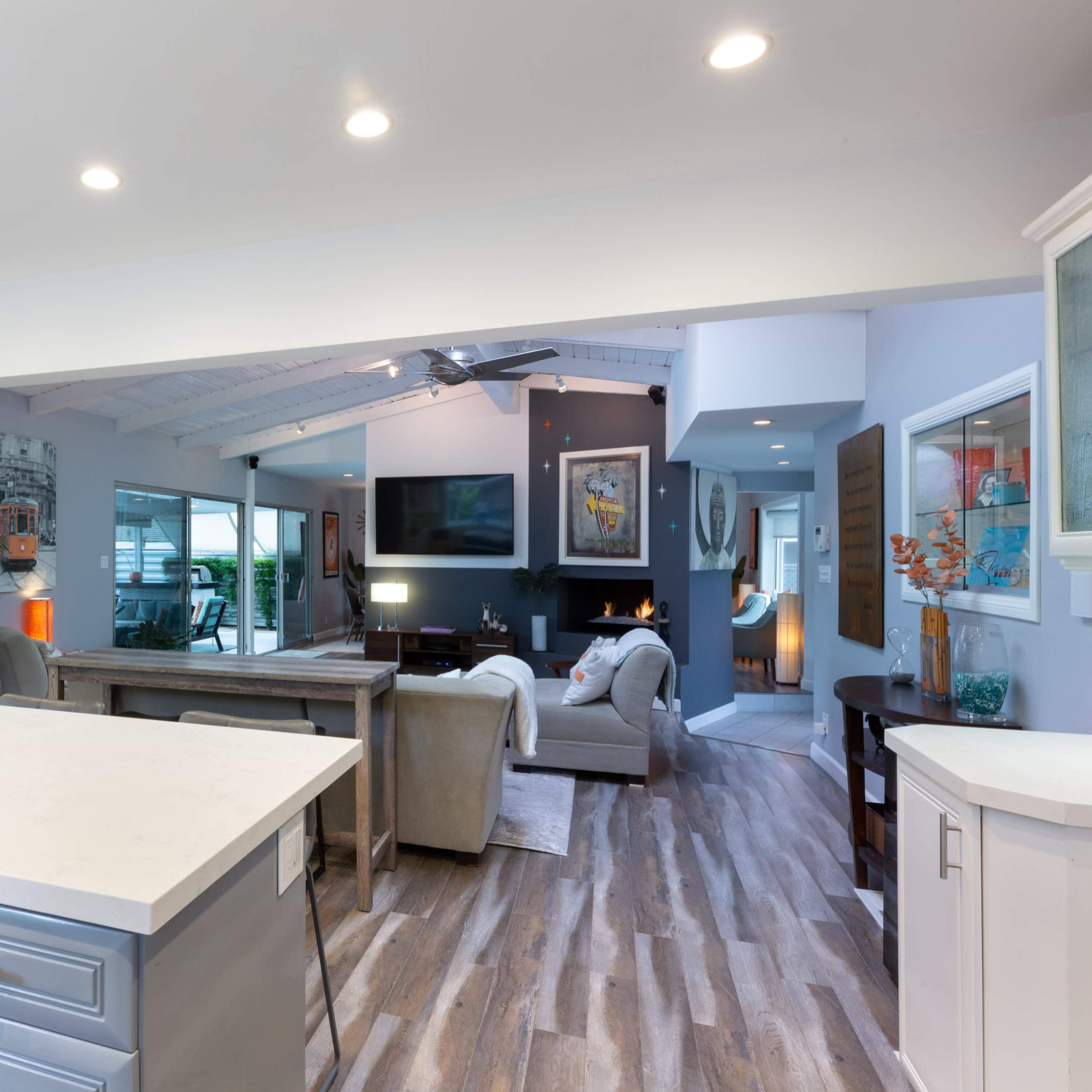 A modern open-concept living space features a kitchen island, dining area, and a cozy seating area with a fireplace, all adorned with neutral tones and natural light.