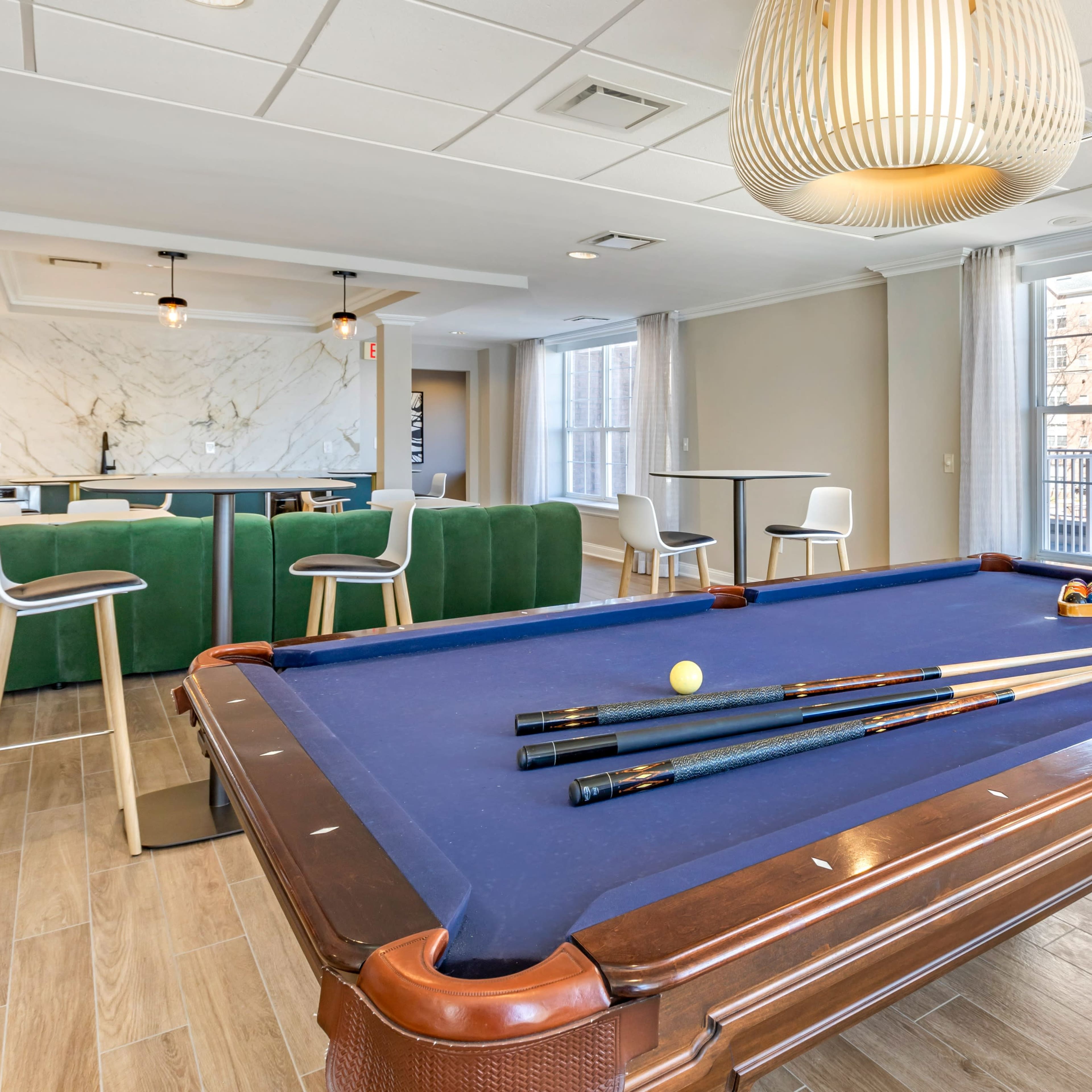 A pool table with cues and balls is set in a modern room featuring a kitchenette and seating area.