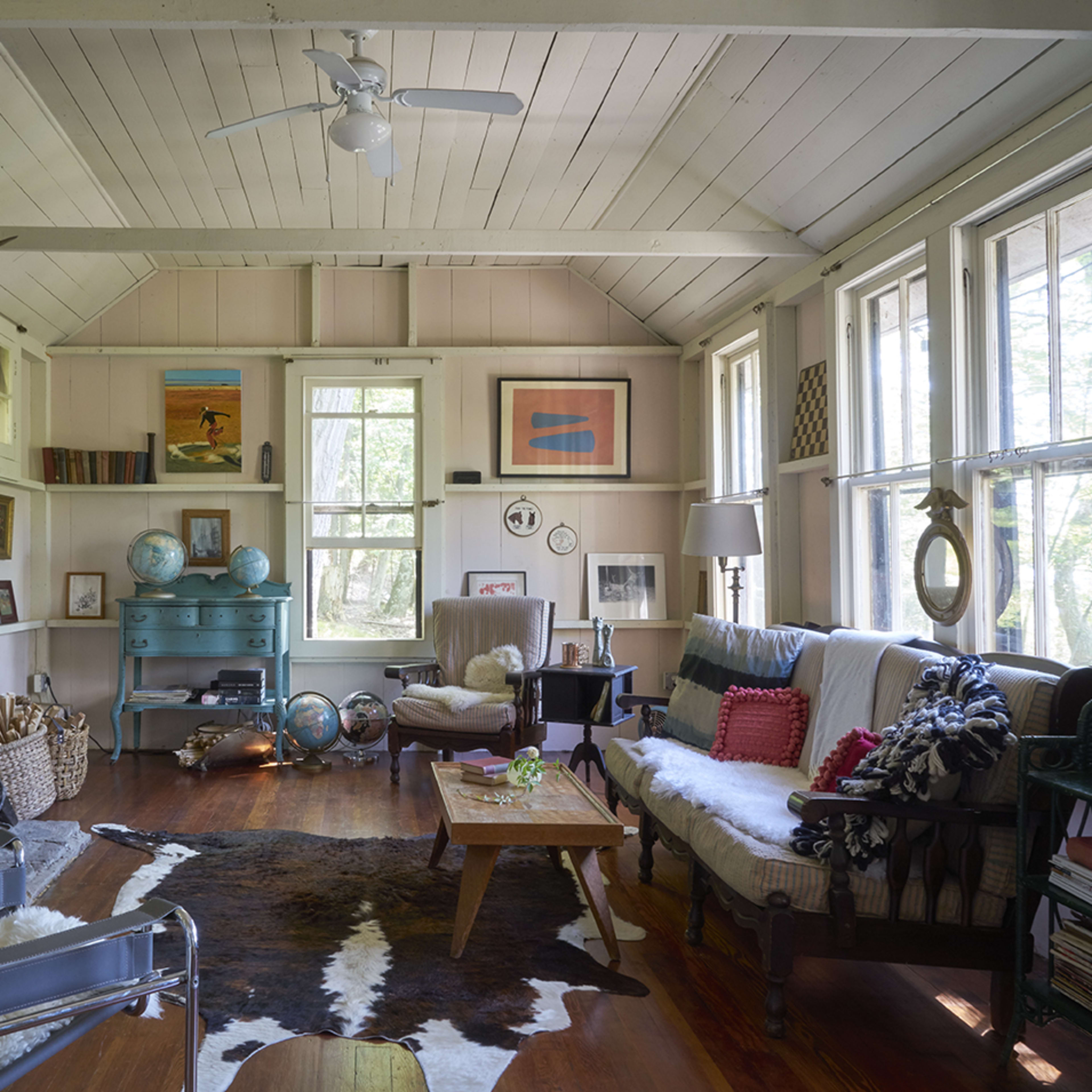 The living room features a stone fireplace, large windows, and a mix of comfortable furniture, including a sofa and armchairs, arranged around a wooden coffee table.