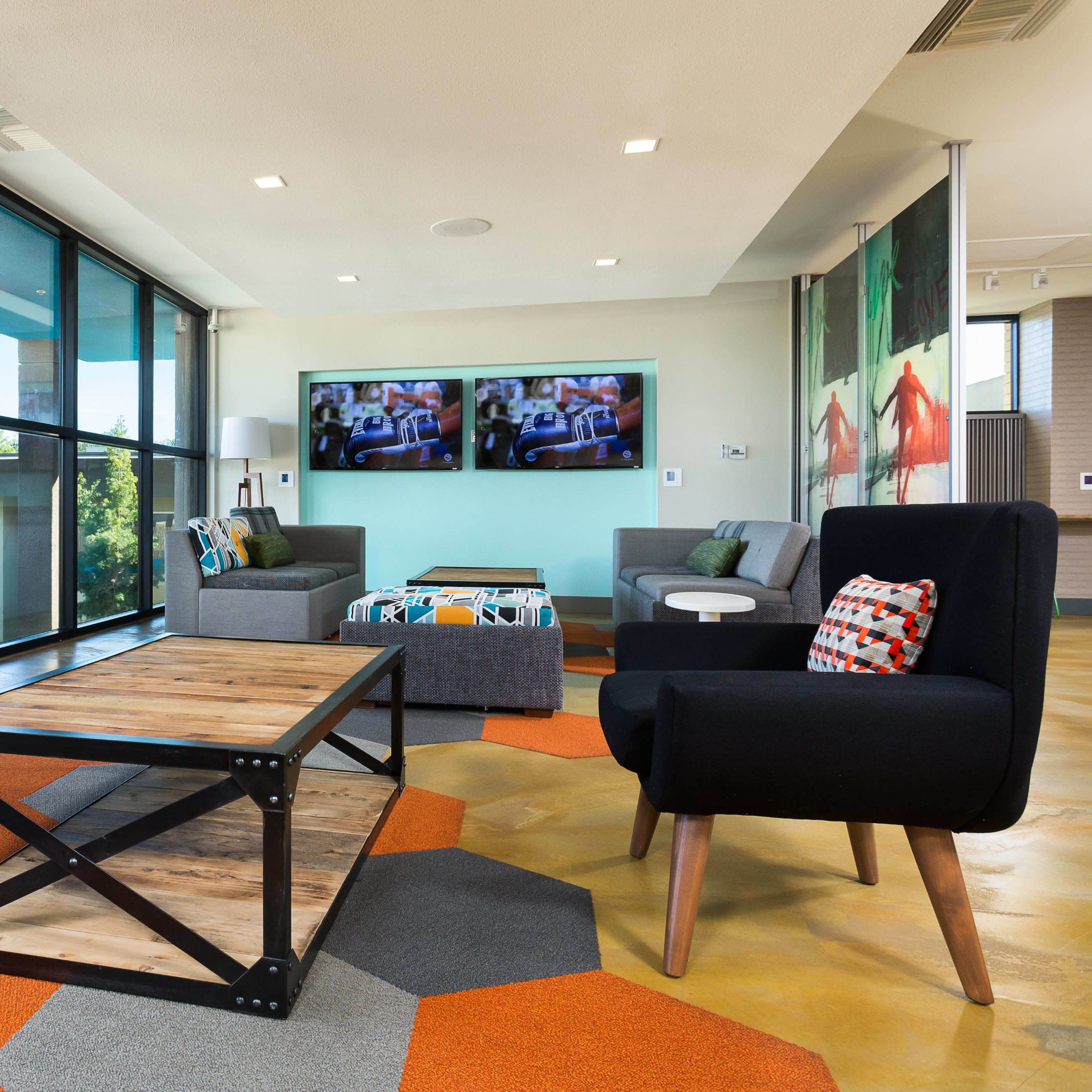 A modern lounge area with large windows, a coffee table, and various seating arrangements, including black armchairs and a gray sofa.