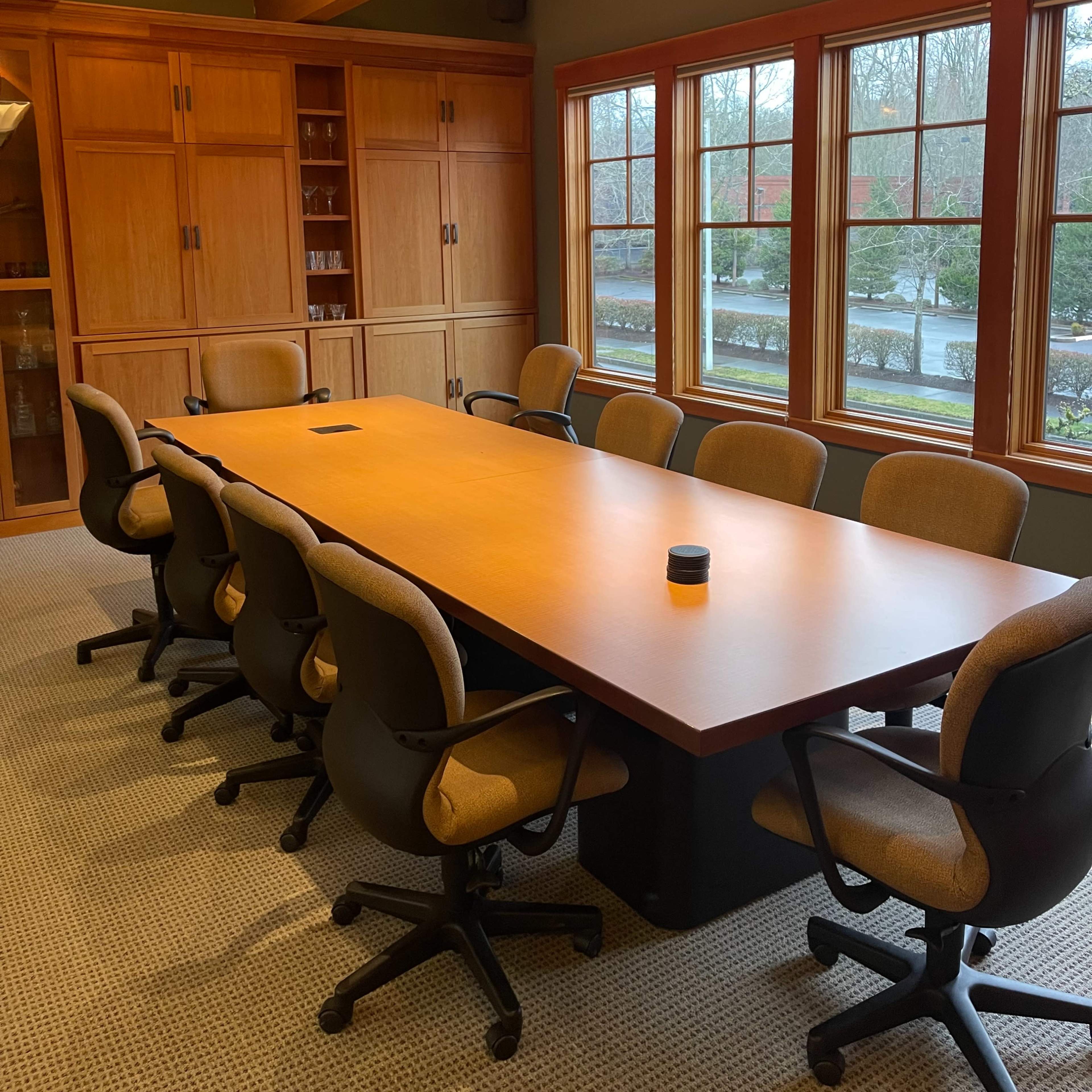 A spacious conference room features a long wooden table surrounded by ergonomic chairs, with large windows providing natural light.
