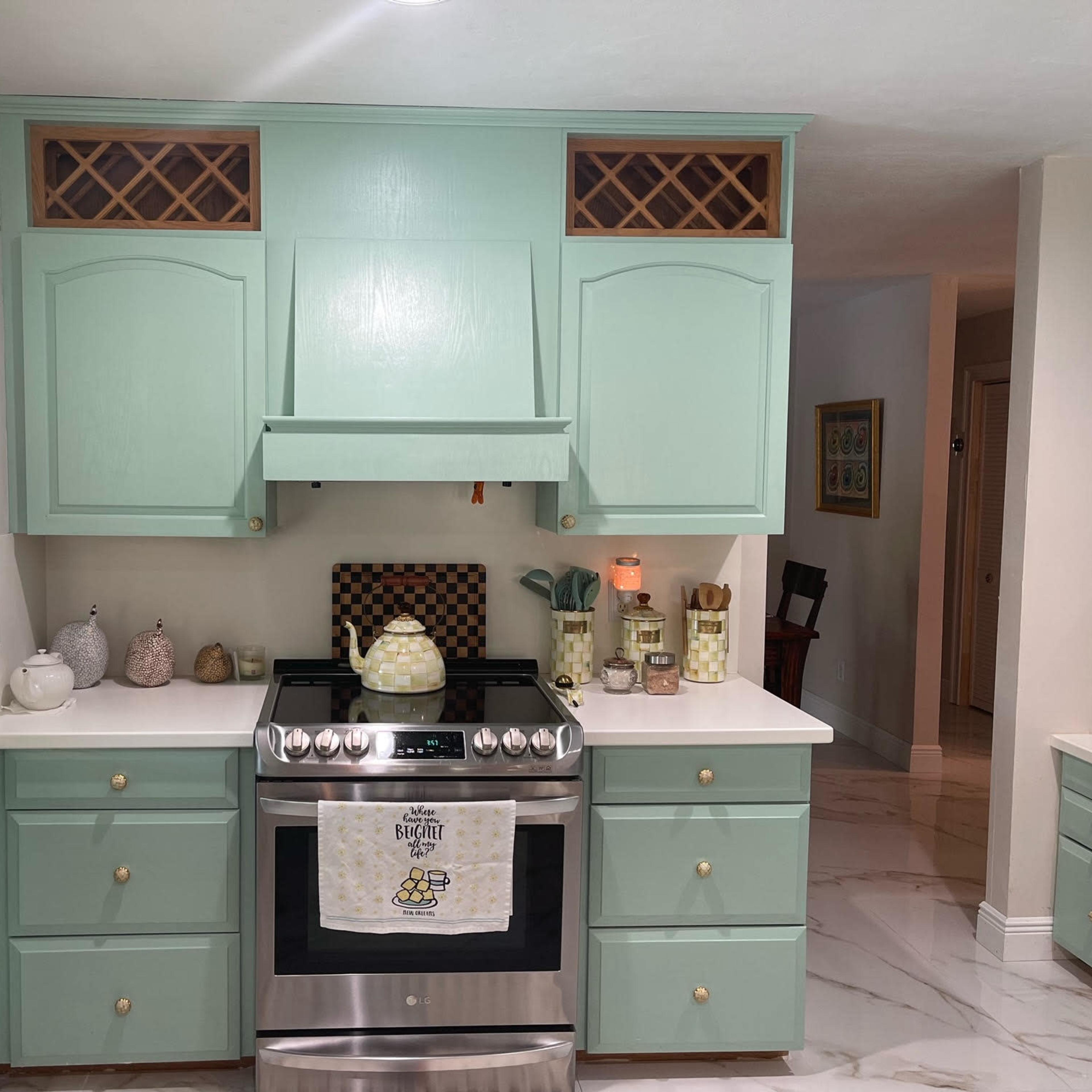 A kitchen with mint green cabinetry, a stainless steel stove, and decorative items on the countertops.