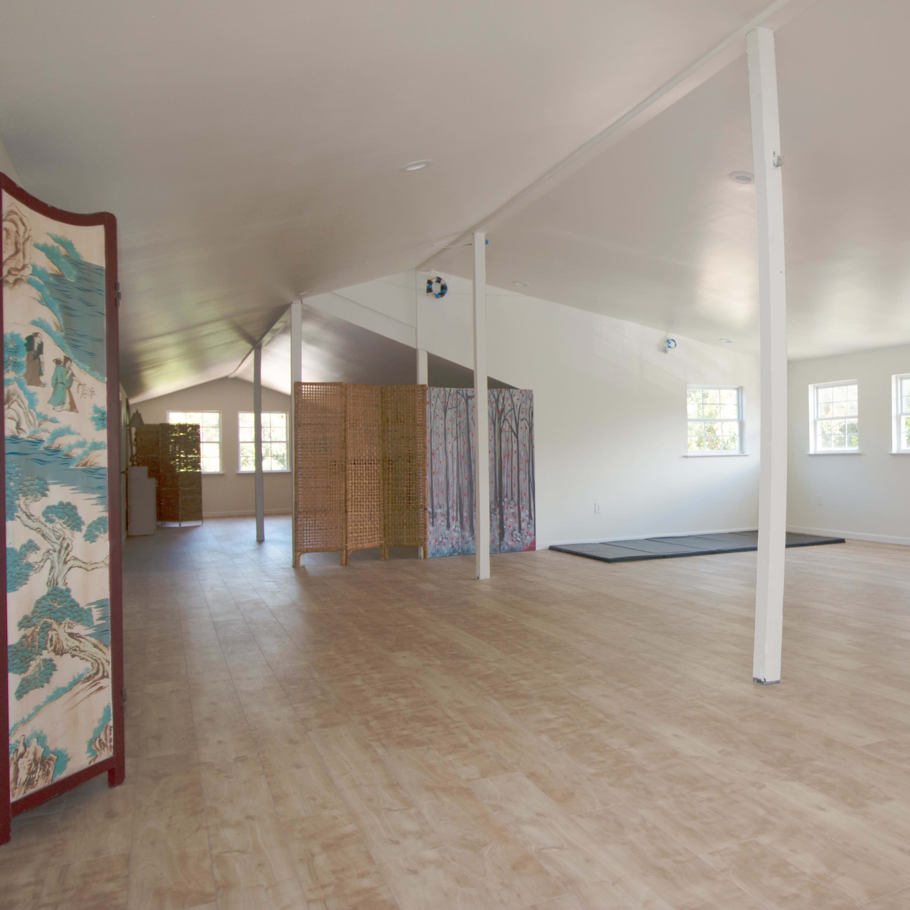 A spacious, bright room with wooden flooring, featuring a few partitions and exercise mats.