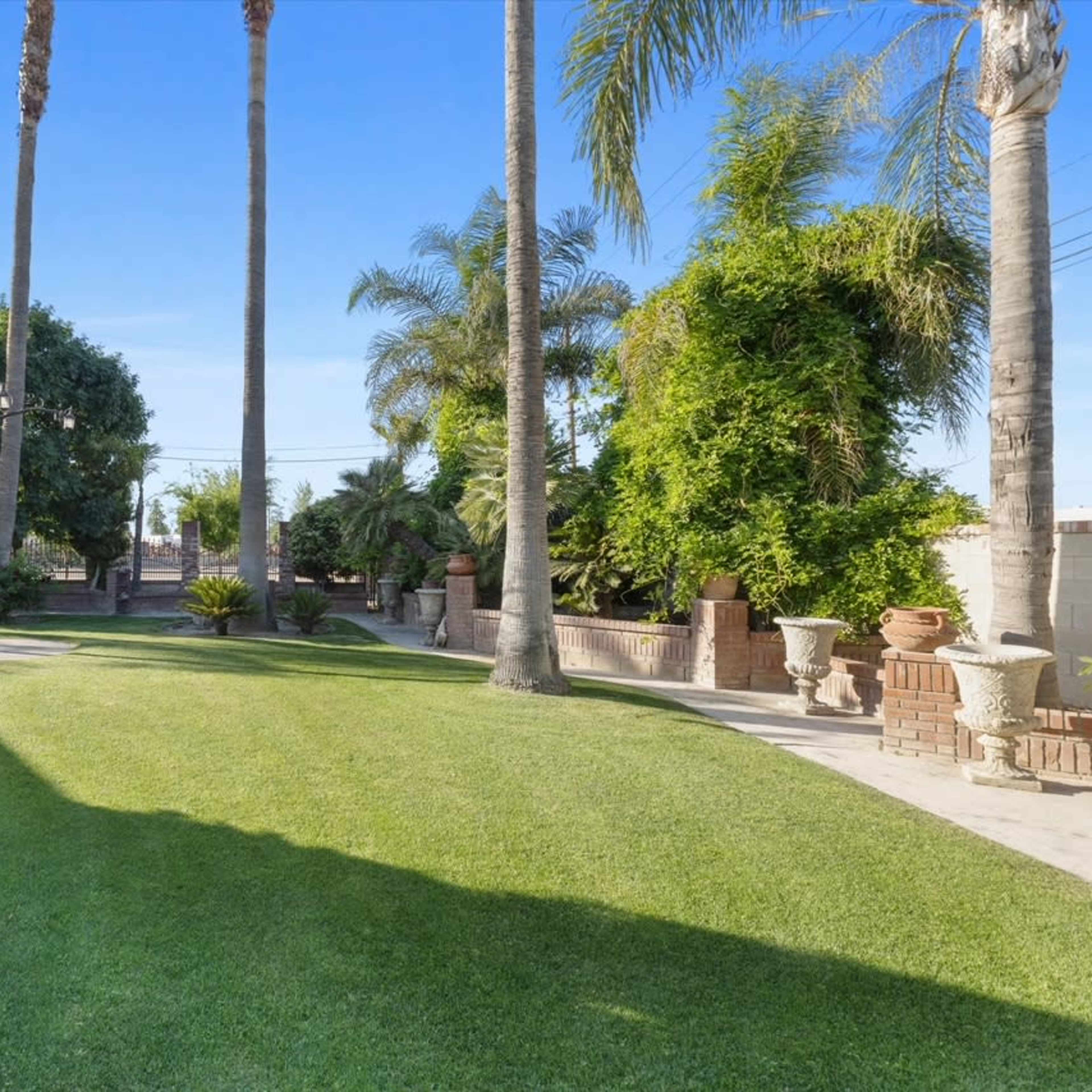 A landscaped backyard with green grass, palm trees, and potted plants along a pathway.