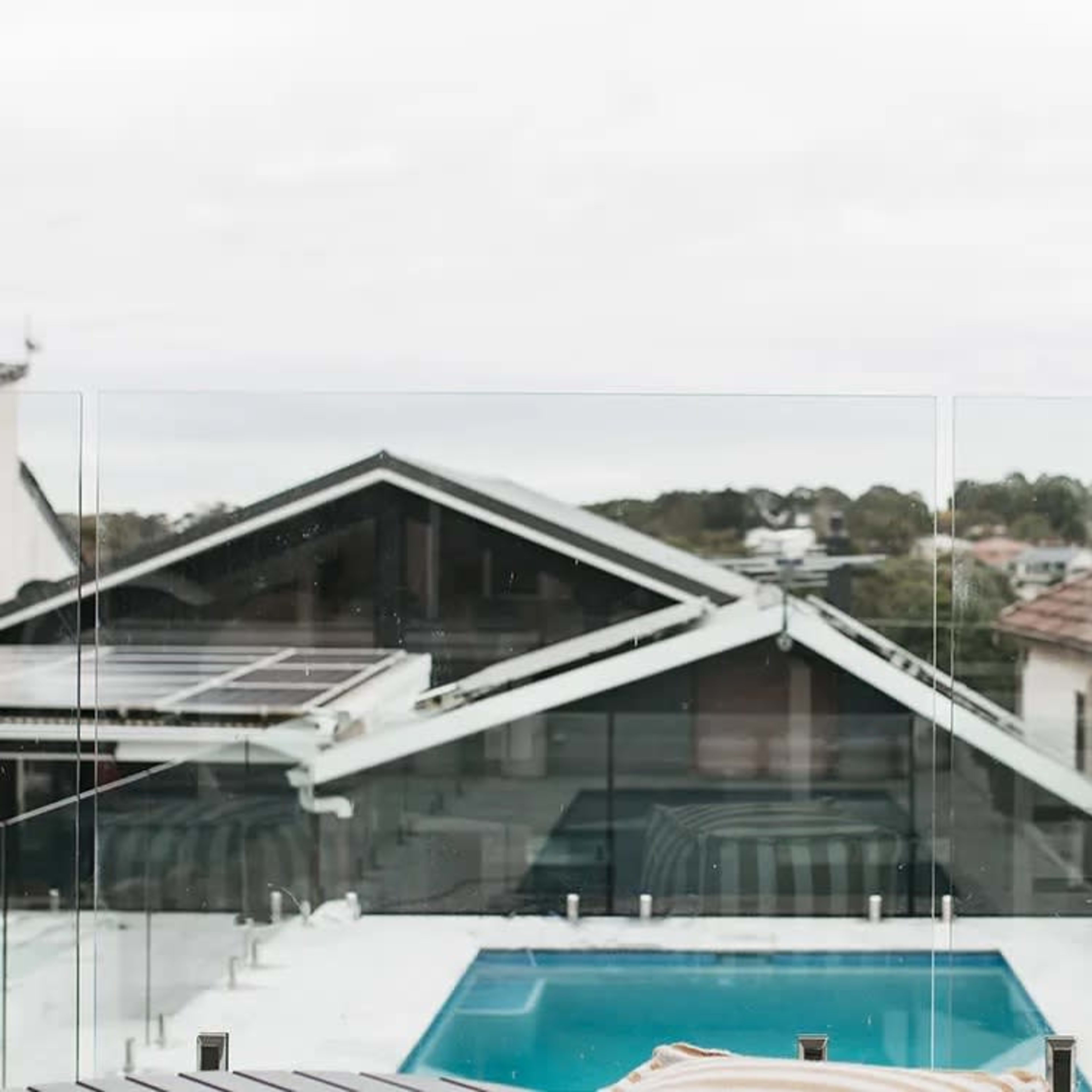 A modern rooftop terrace with a pool and potted cactus, framed by a glass railing and overlooking residential buildings.