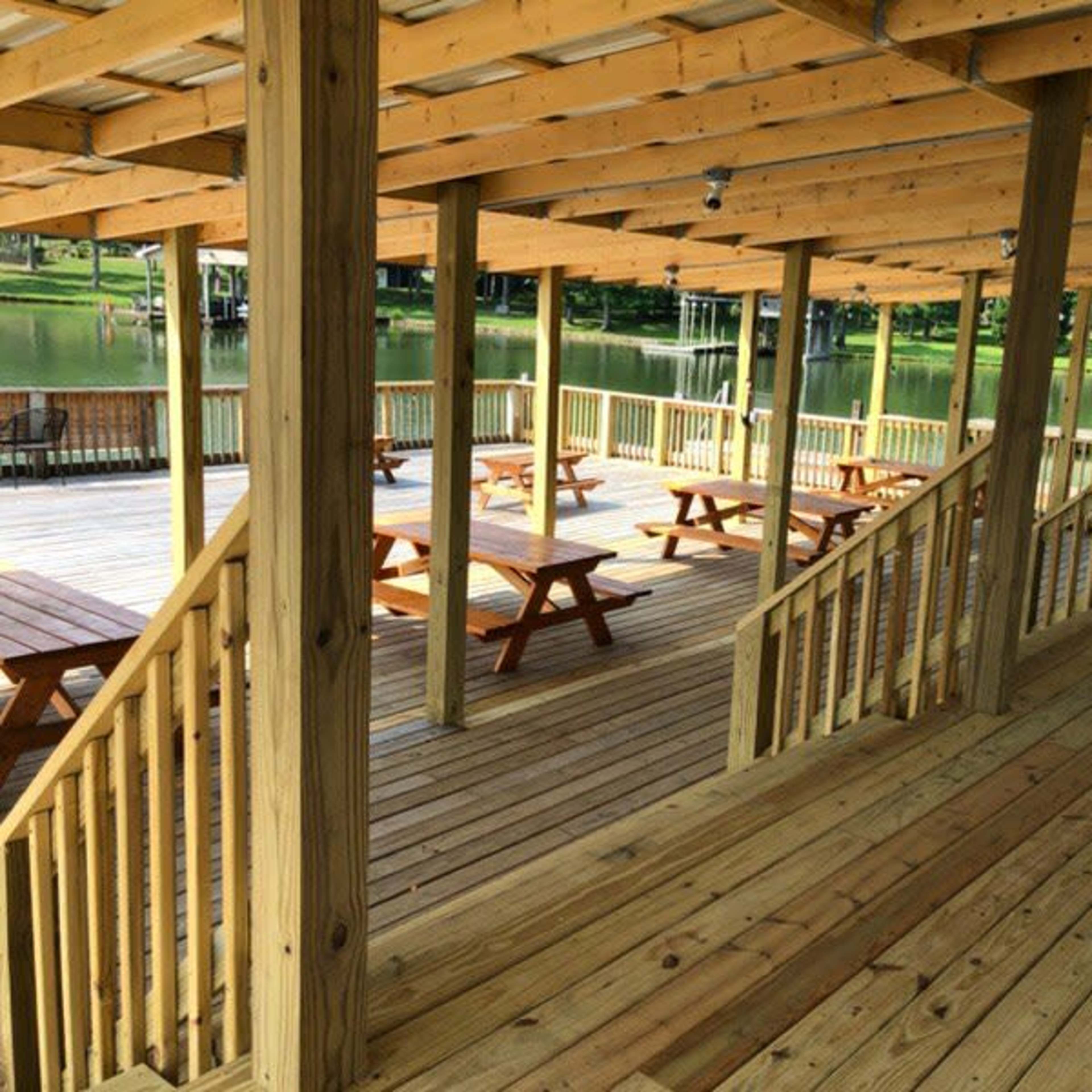 A wooden pavilion with picnic tables and stairs, overlooking a body of water.