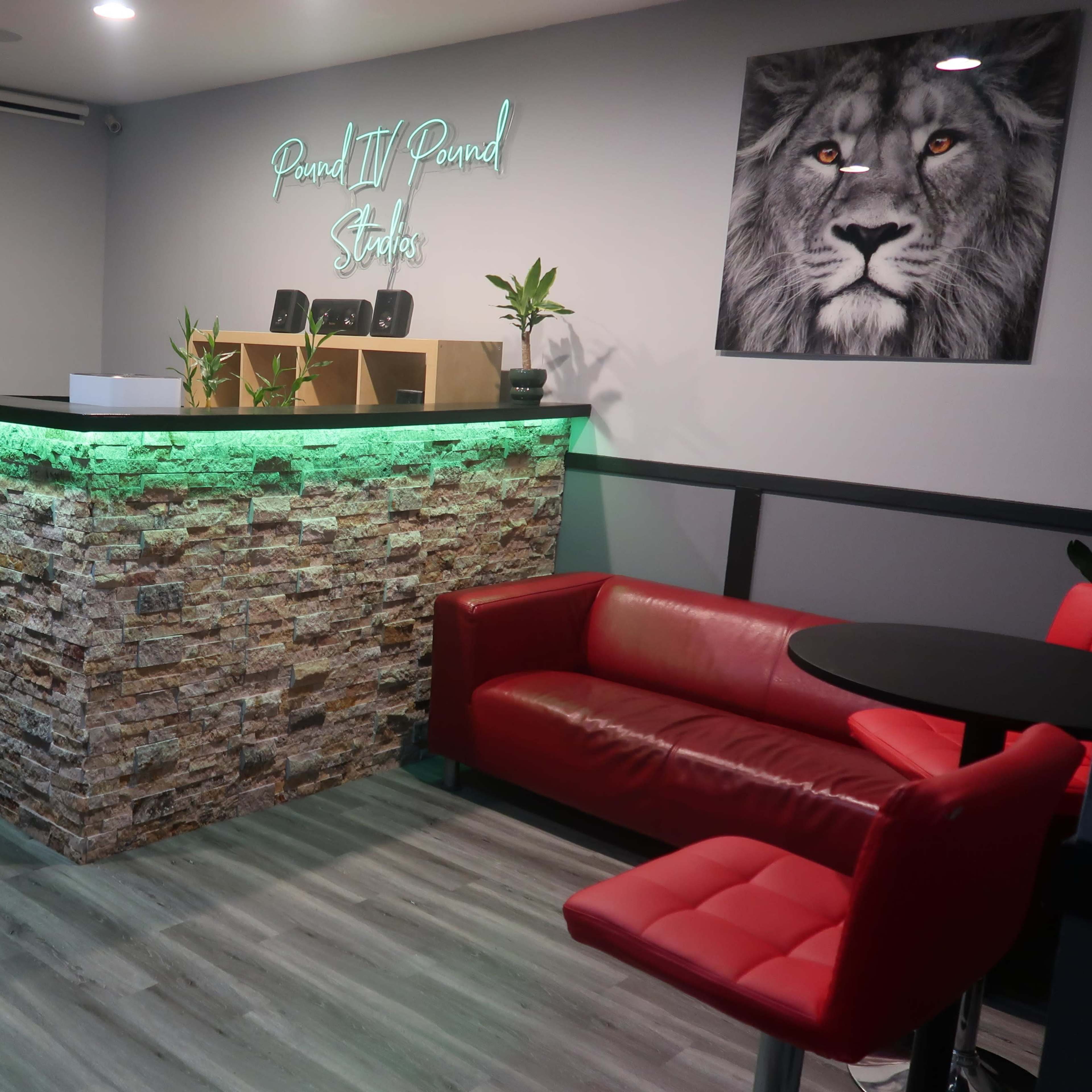 A modern studio reception area with a stone-patterned front desk illuminated by green lights, furnished with a red sofa and a black table.