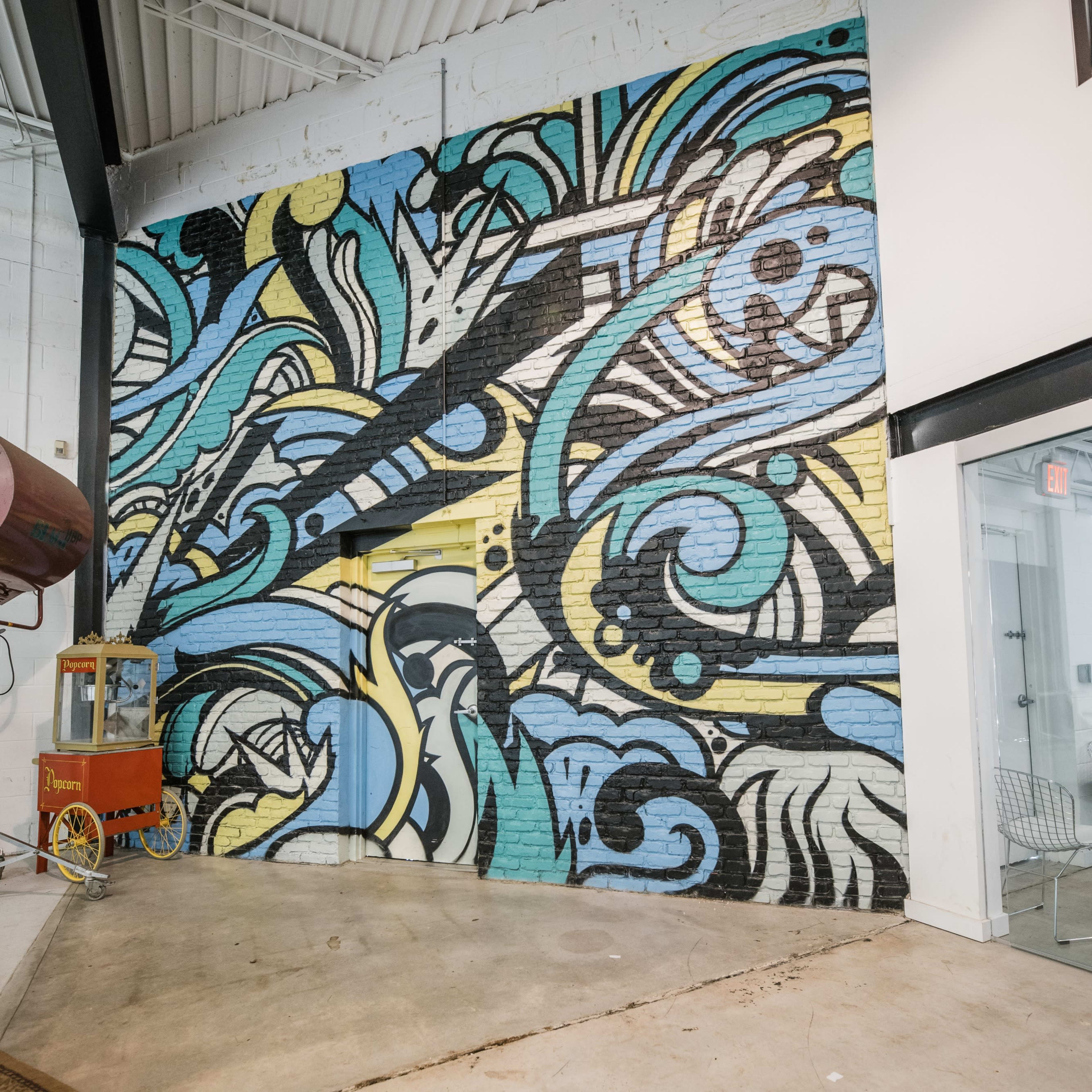 A colorful mural featuring abstract swirls and shapes covers a brick wall in a spacious interior.