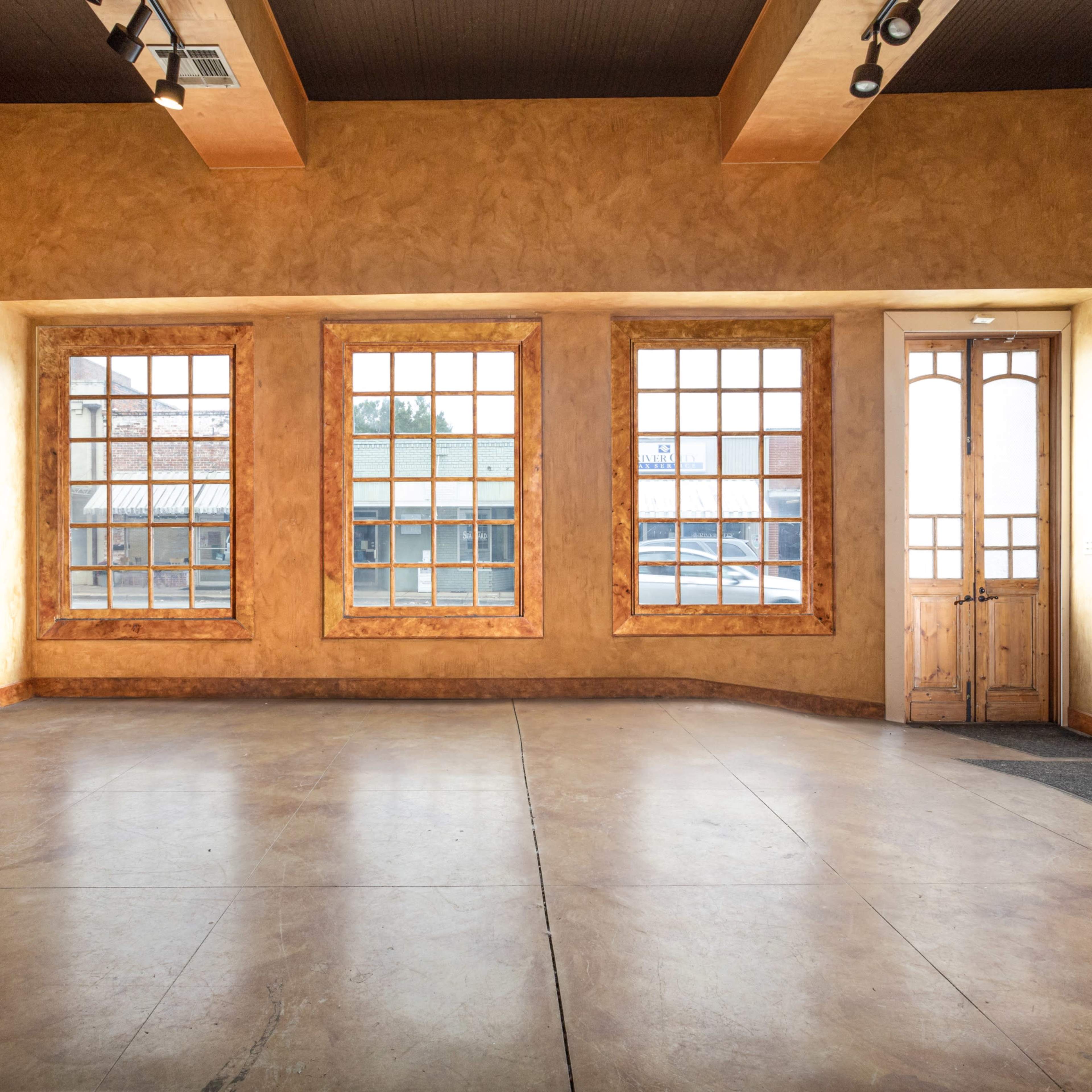 An empty room with exposed brick walls, large windows, and a wooden door leading outside.