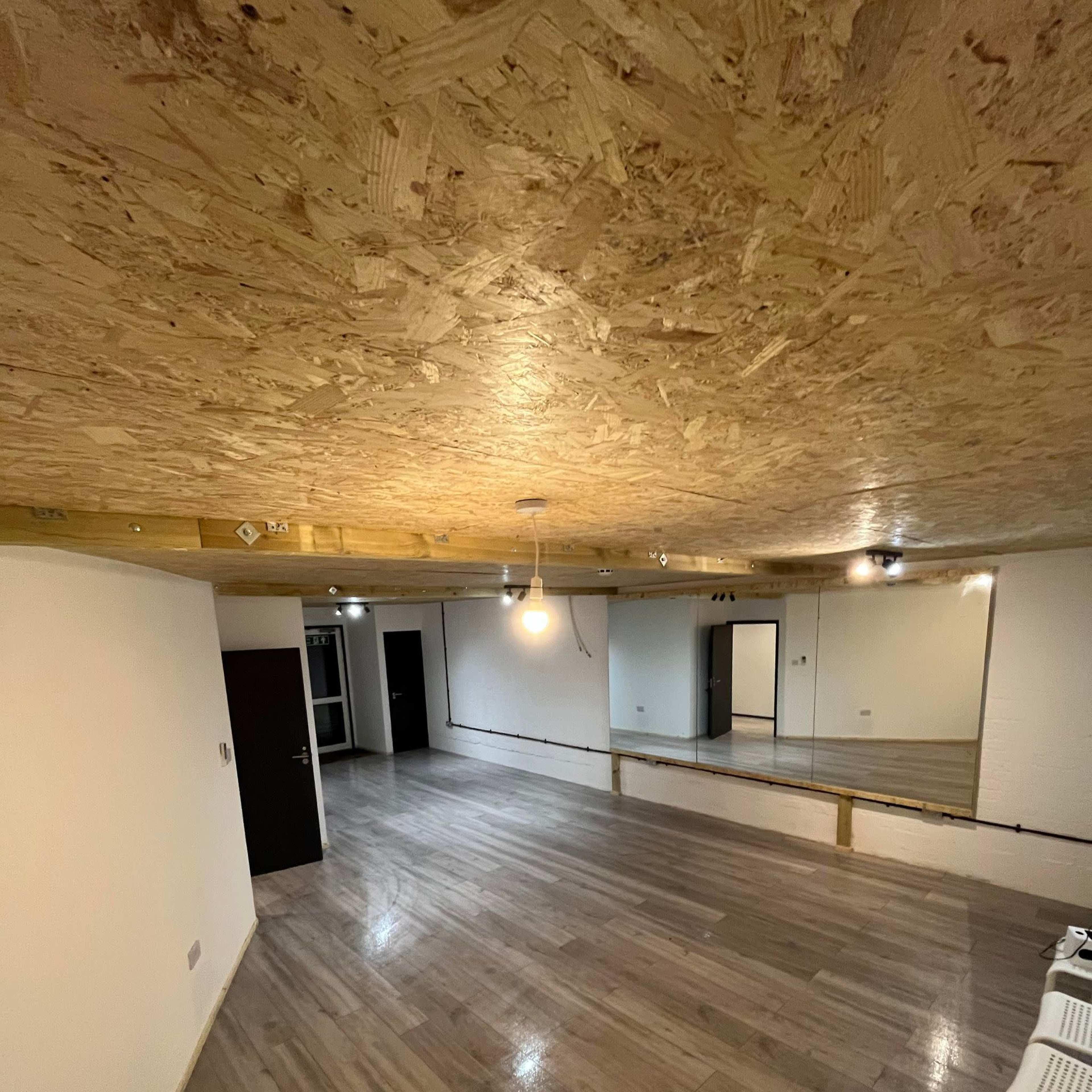 A spacious interior room with a wooden ceiling, wooden floor, and a large mirror along one wall.