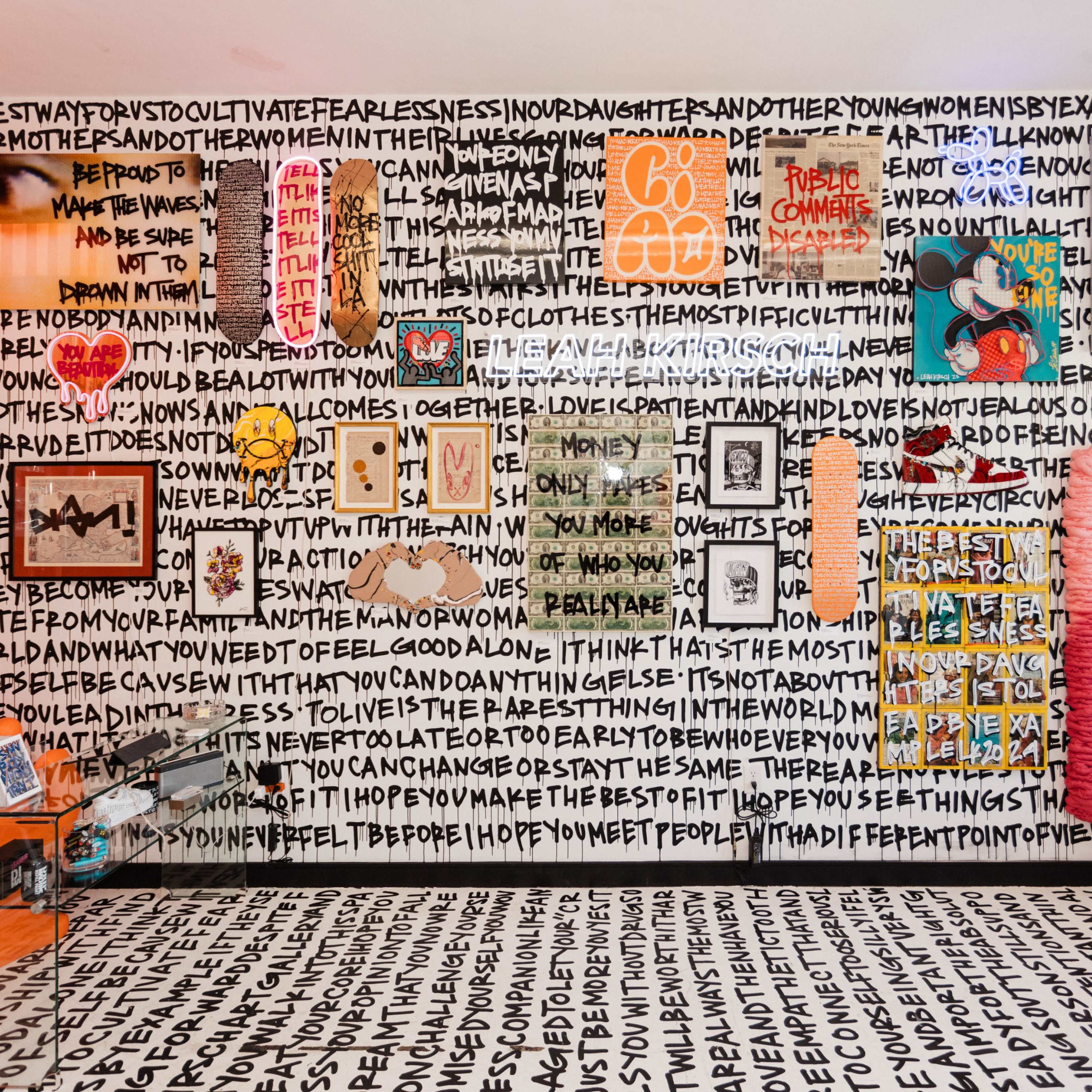 A colorful room with a patterned wall covered in bold, handwritten text and various framed artworks, including photographs and illustrations, arranged along the walls.