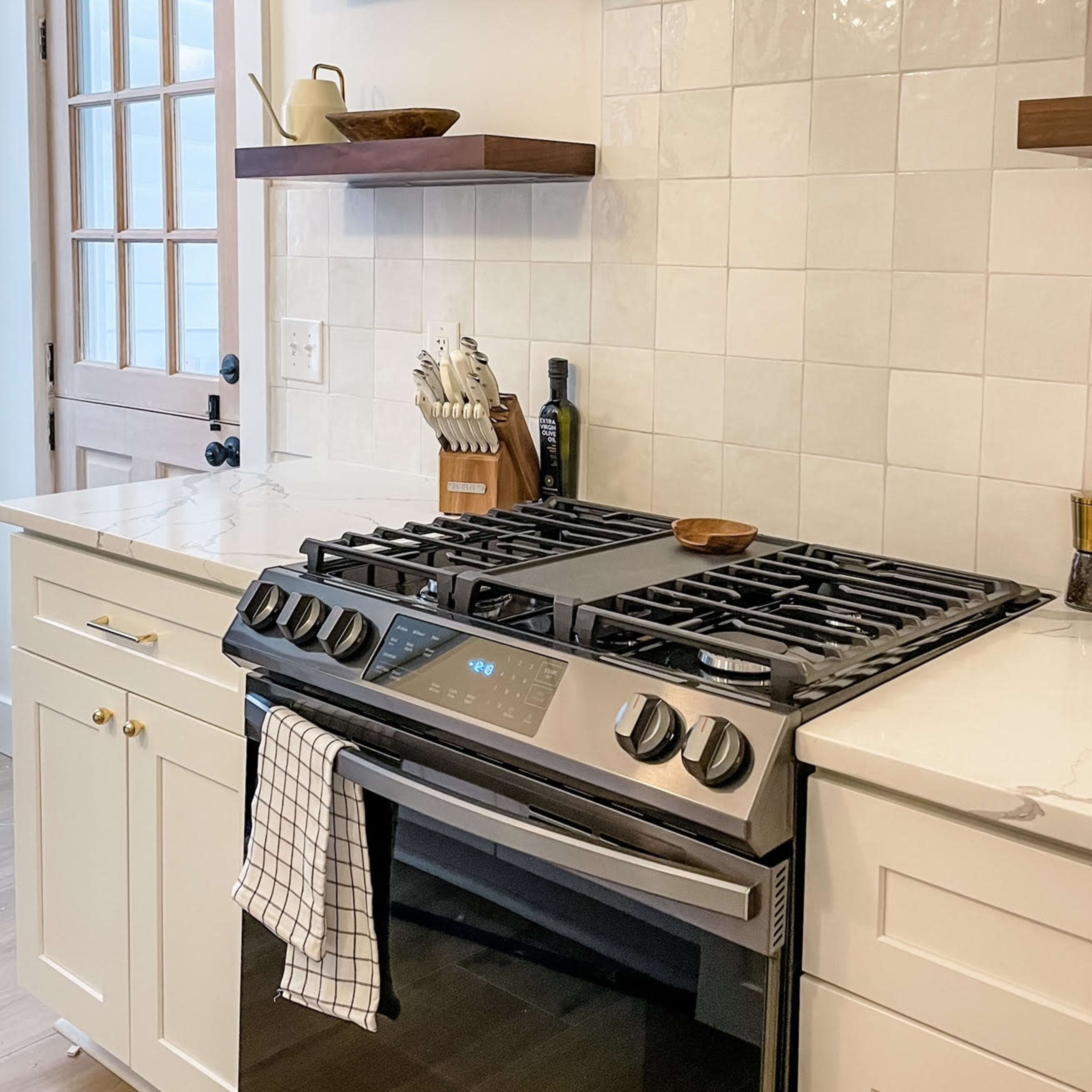 A modern kitchen with a gas stove, hood, and open shelves filled with kitchen utensils and decor.