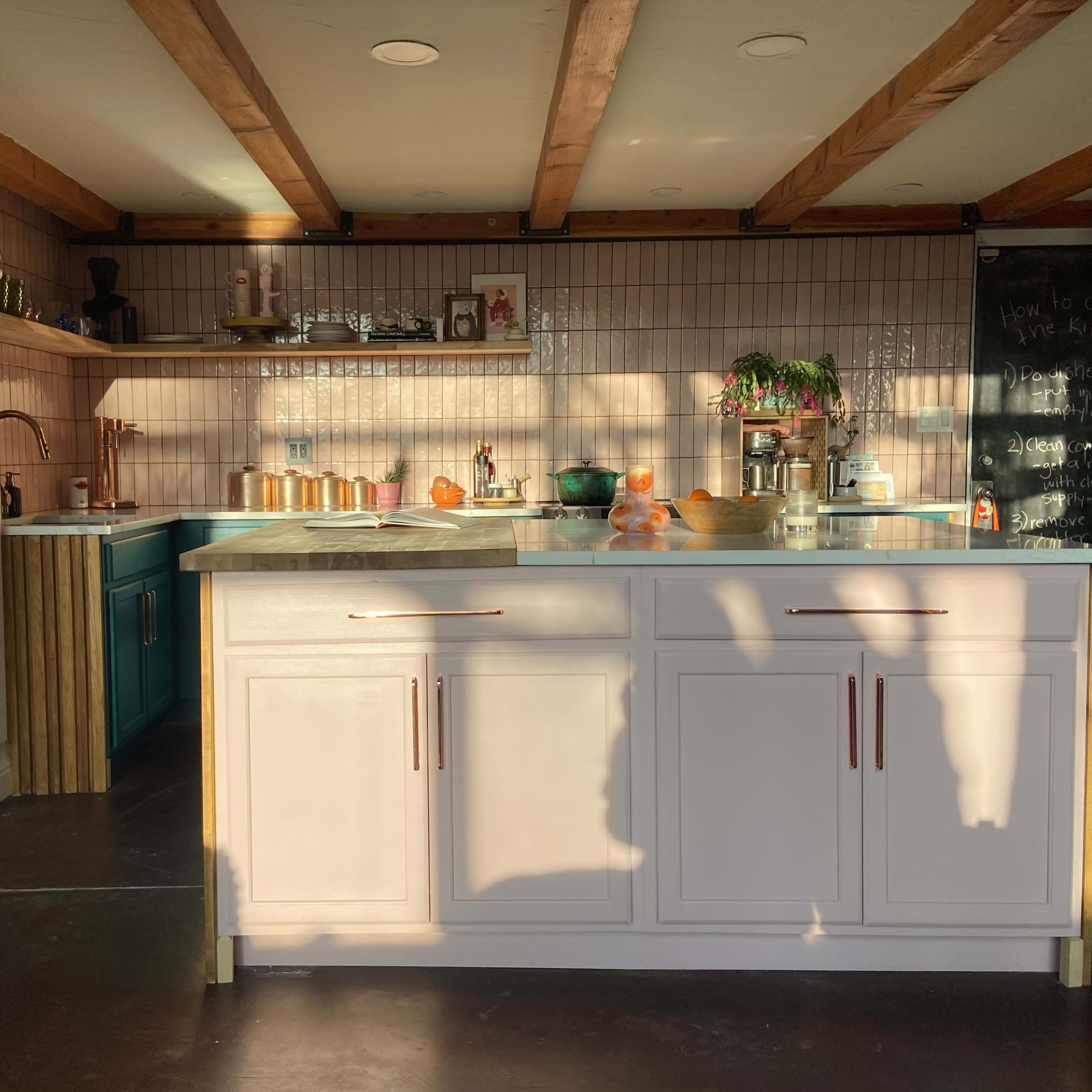 A well-lit kitchen with a white island, wooden beams on the ceiling, and various kitchen items arranged on the counters.