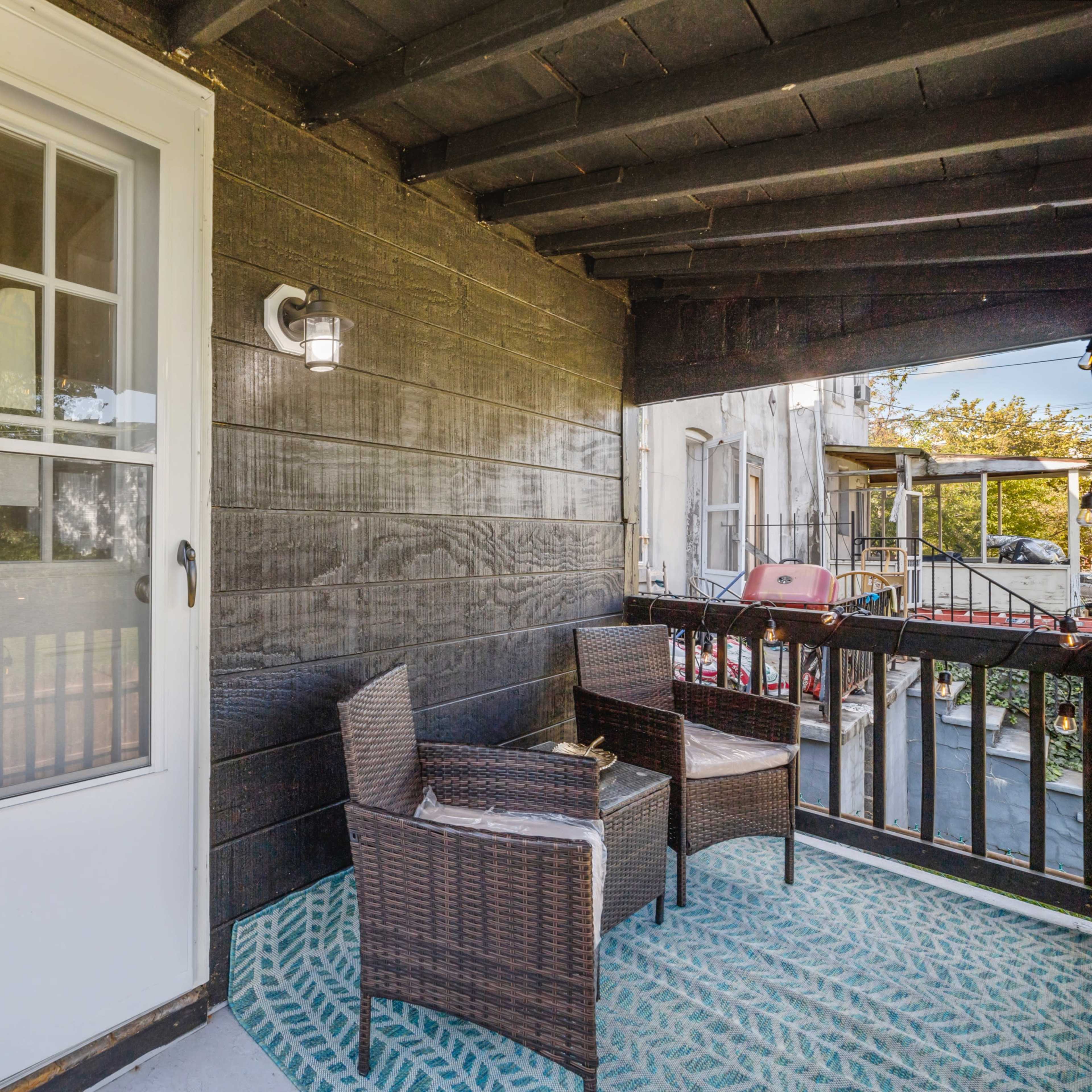 A small balcony features two wicker chairs and a decorative rug in front of a white door.