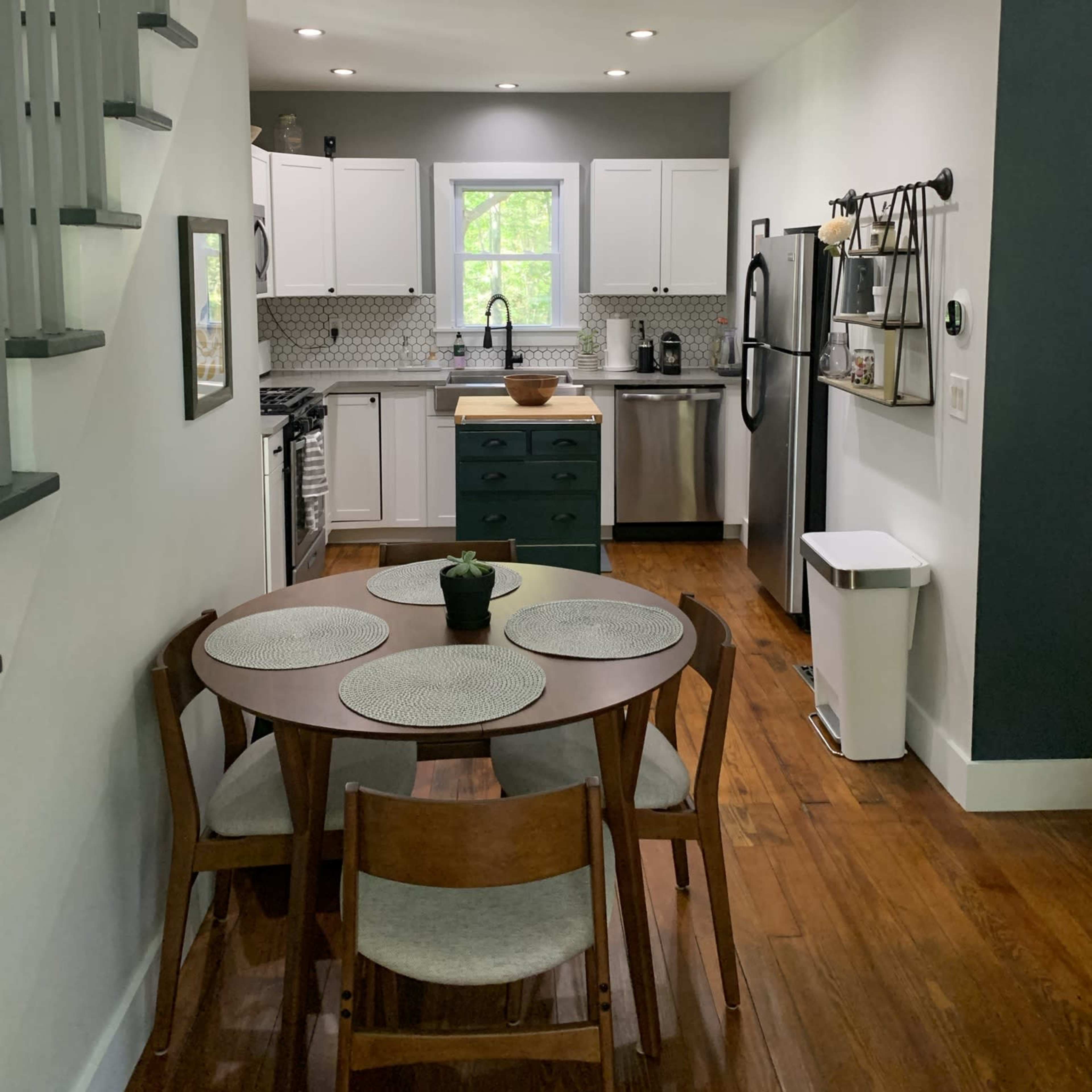 A modern kitchen featuring white cabinets, a green island, a stainless steel refrigerator, and a wooden dining table with four chairs.