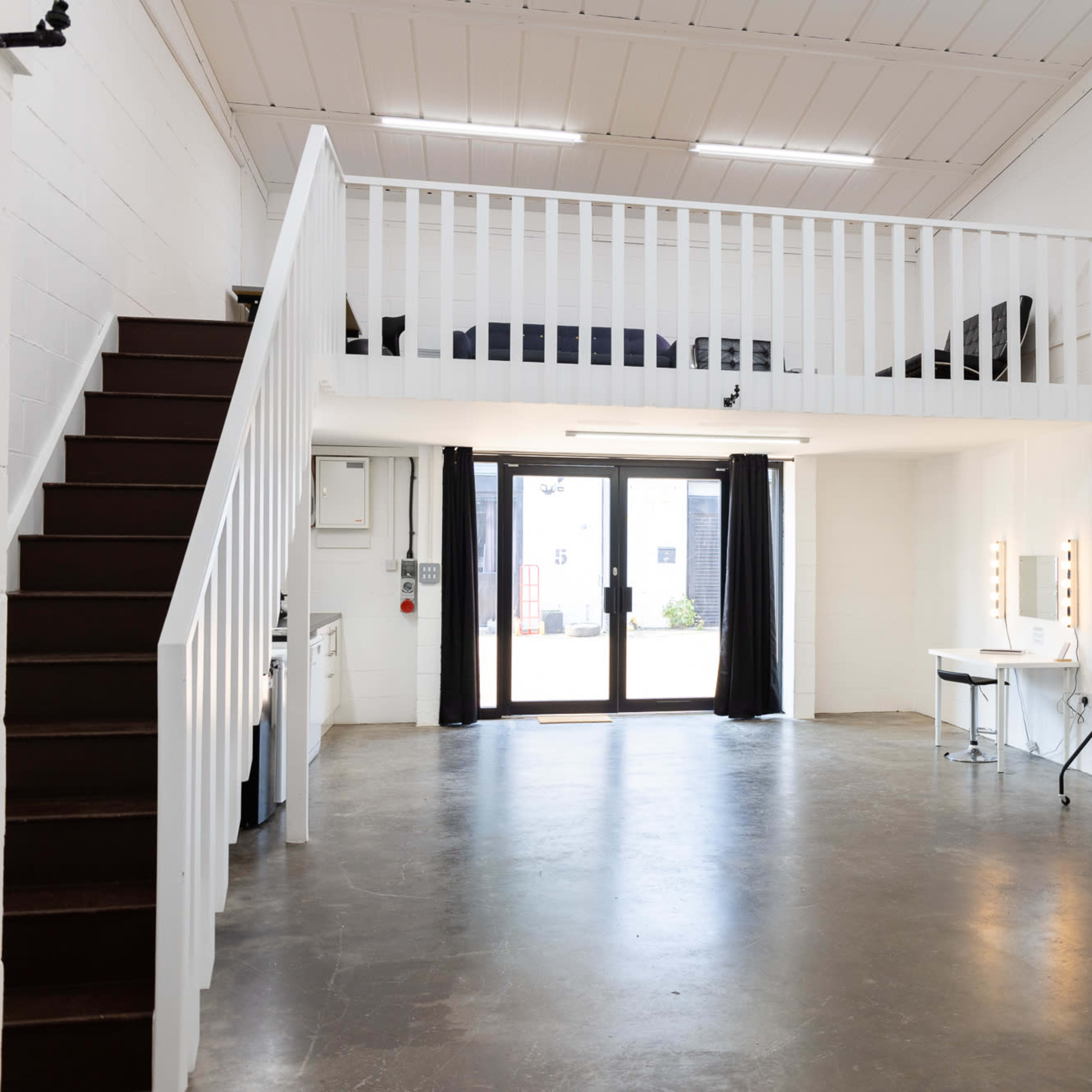An open interior space with a loft area, a staircase, and a large glass door leading outside.
