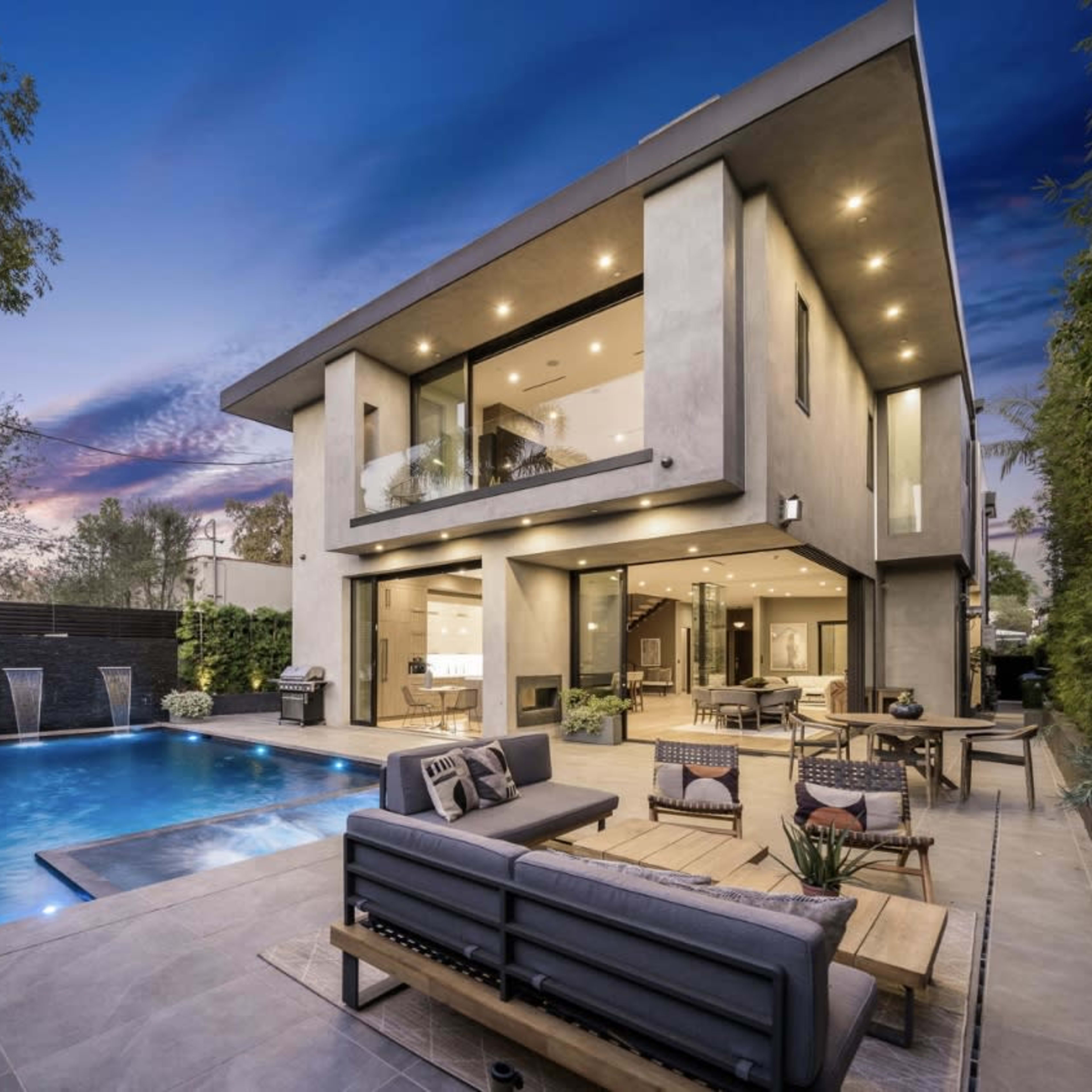 A modern two-story house with large windows and a swimming pool surrounded by a landscaped outdoor area.