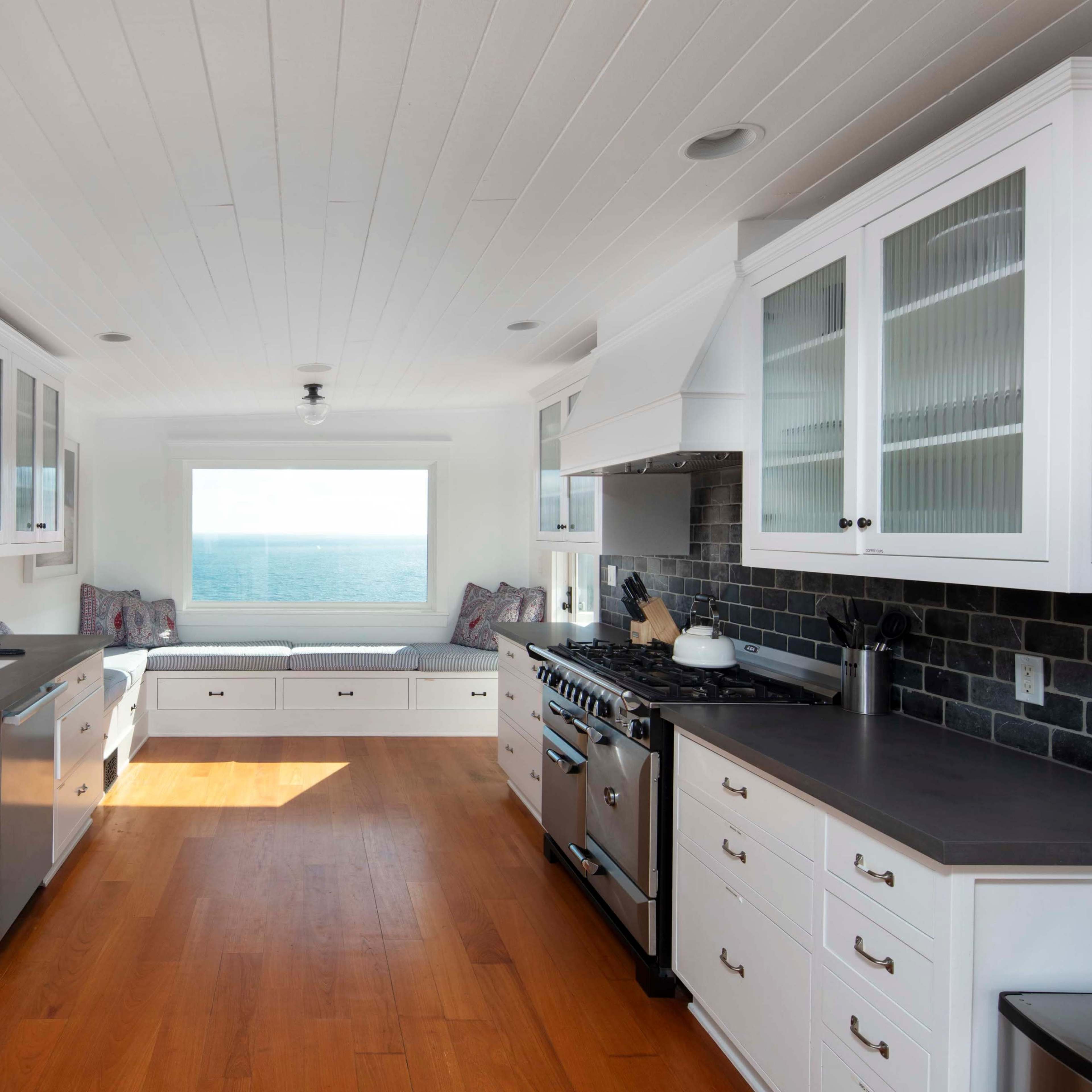 The kitchen features white cabinetry, a large window with ocean views, and a seating area by the window.