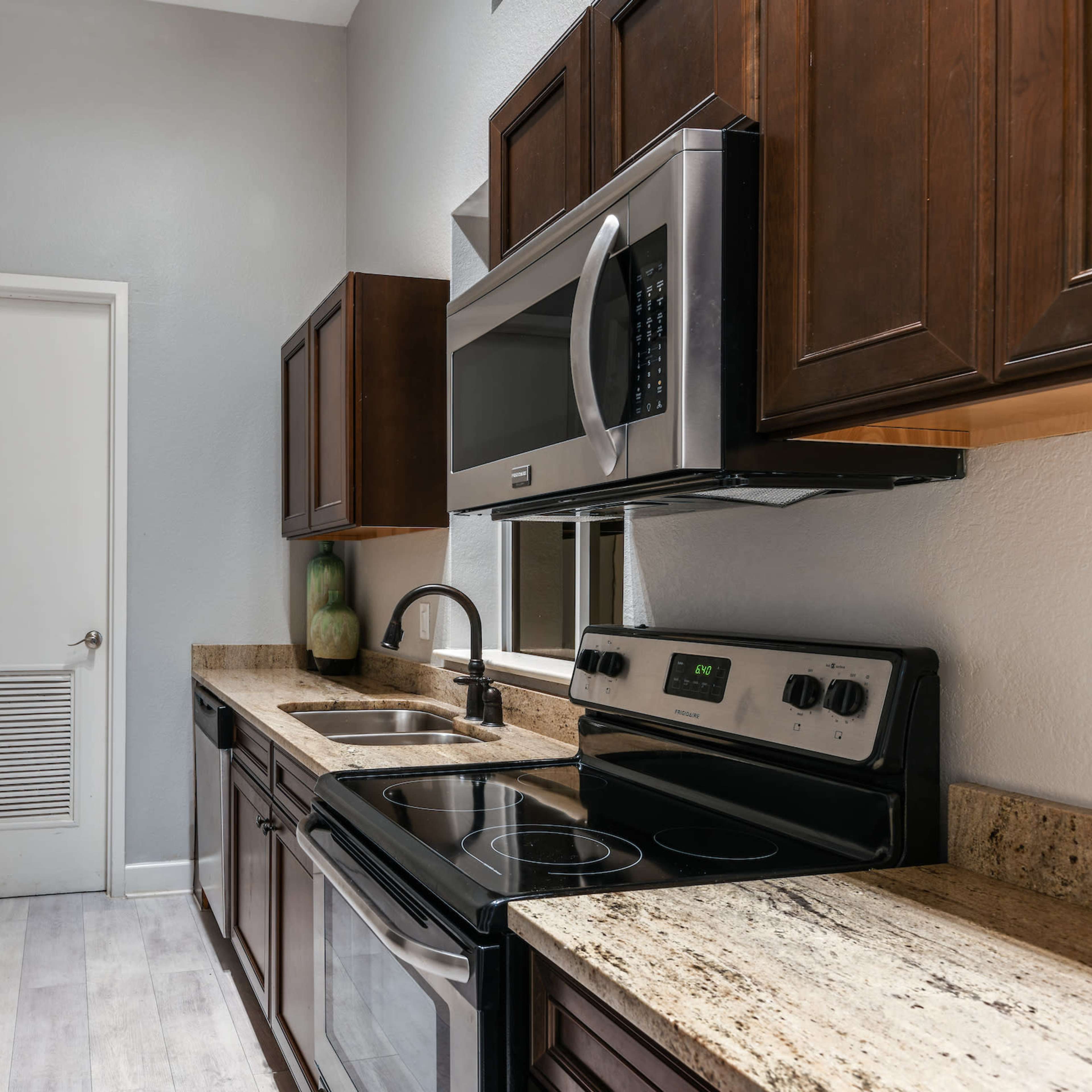 A modern kitchen featuring stainless steel appliances, dark wooden cabinets, and a granite countertop.