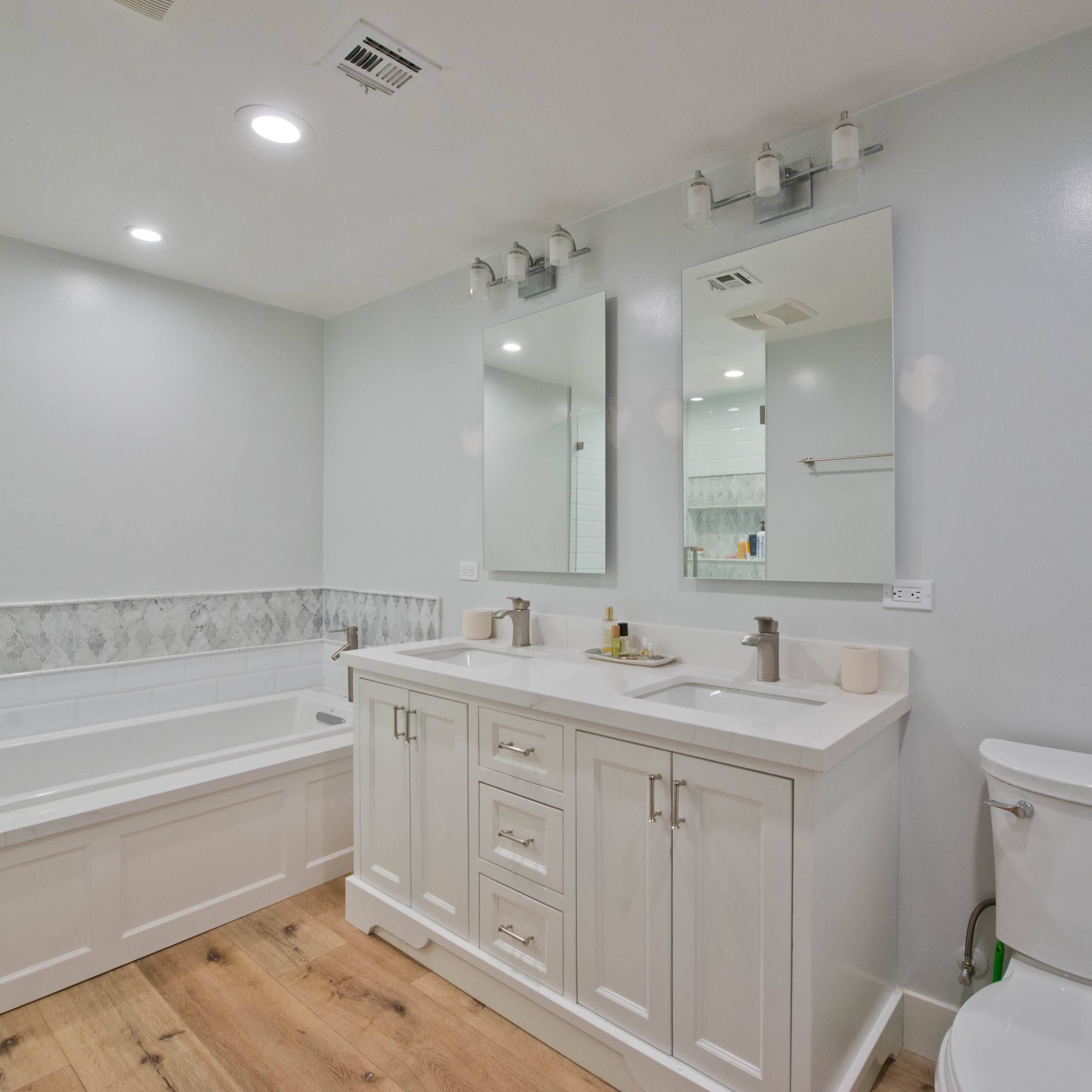A modern bathroom featuring a double sink vanity, a bathtub, and white tiled walls.