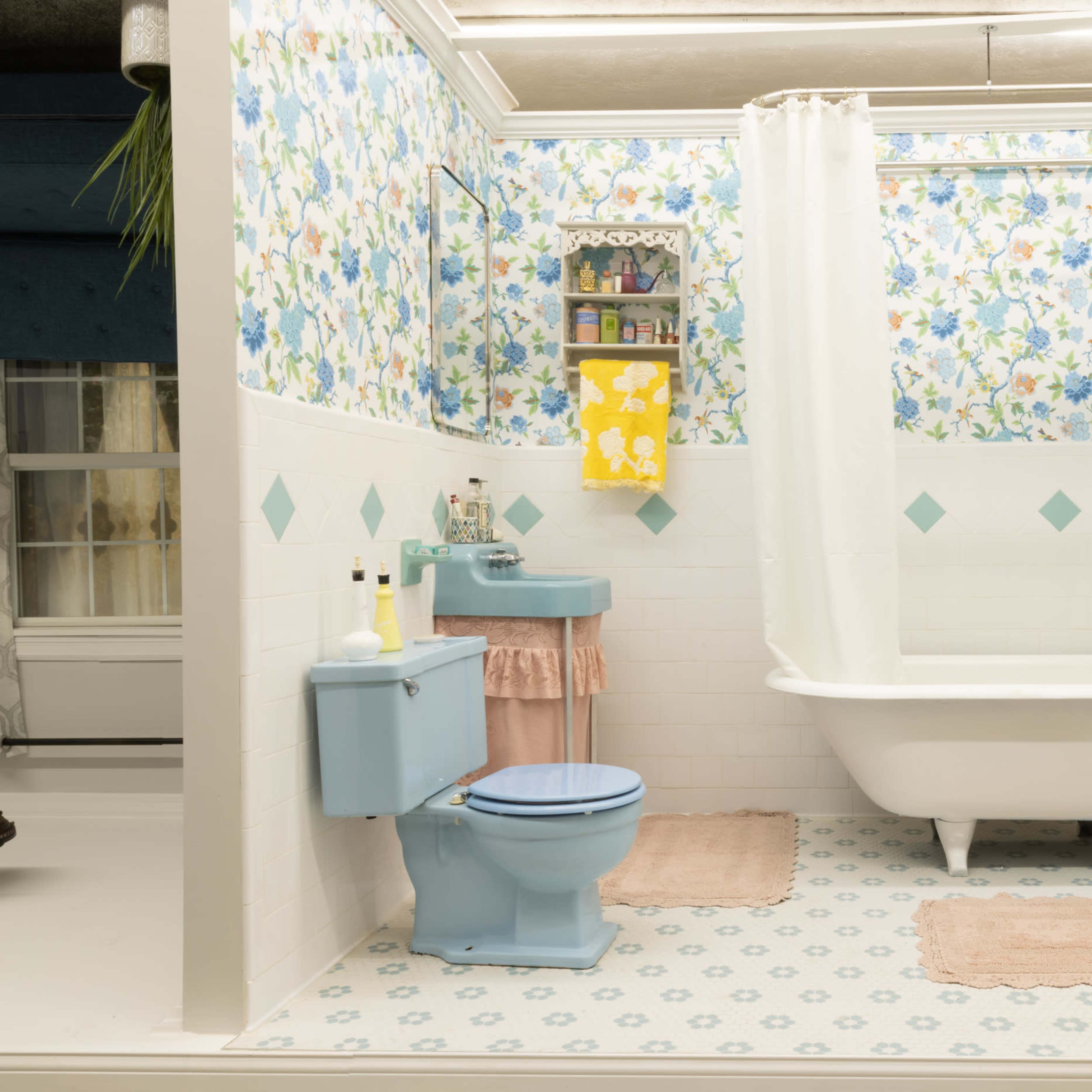 A bathroom featuring a clawfoot bathtub, a toilet, and floral wallpaper with decorative towels and mats.