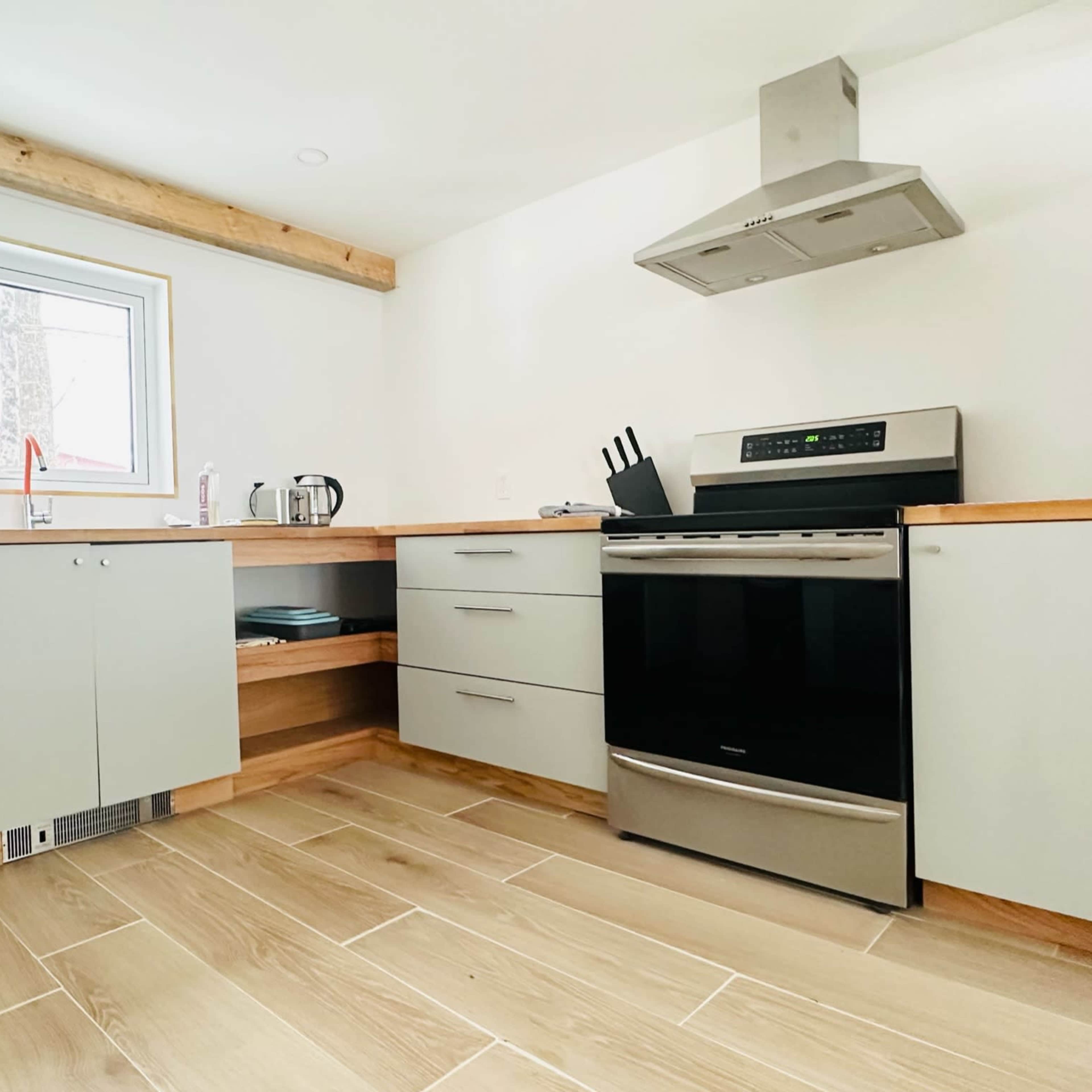 A modern kitchen with gray cabinets, a stainless steel stove, and a window overlooking a wooded area.