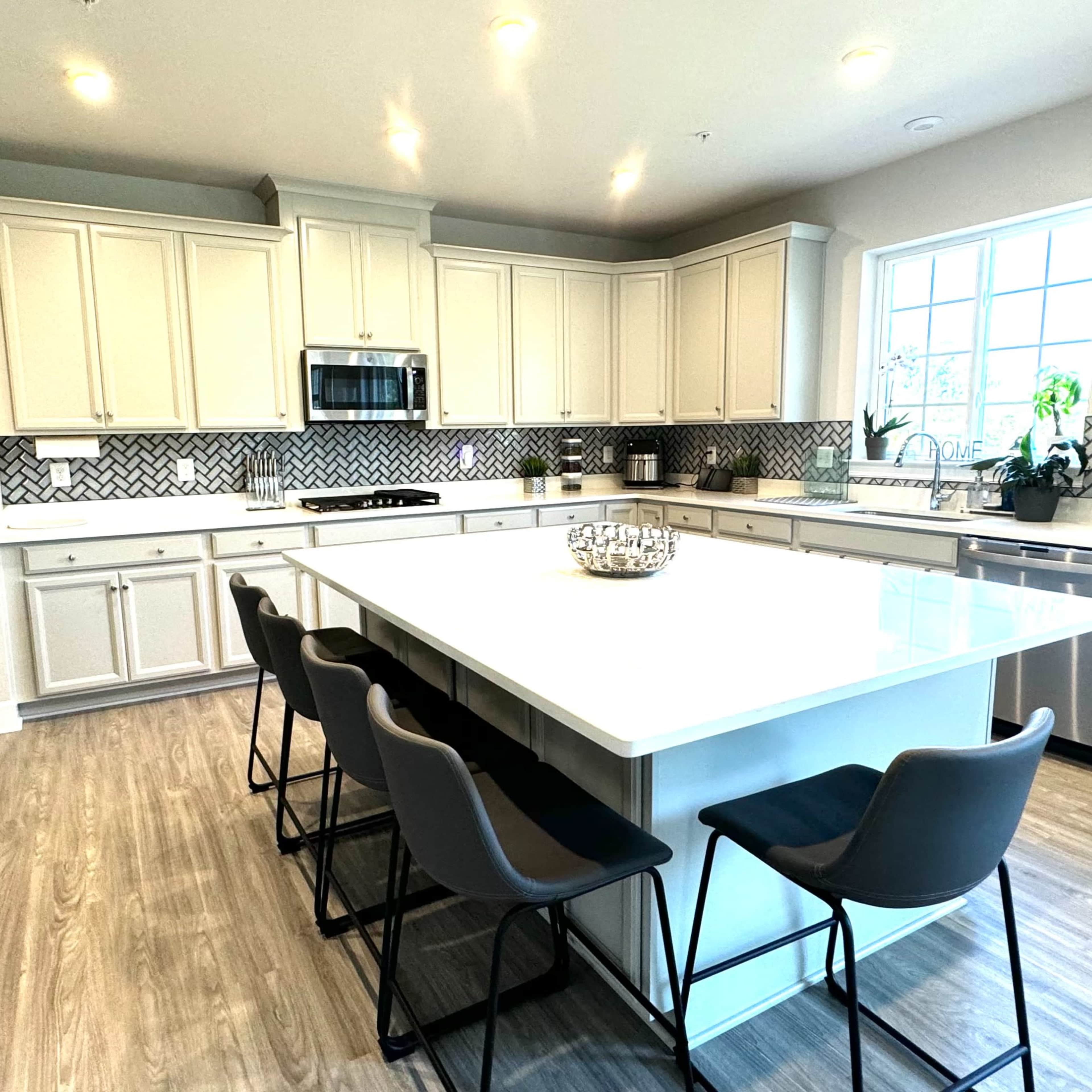 A modern kitchen with white cabinets, a large island with seating, and a herringbone-patterned backsplash.