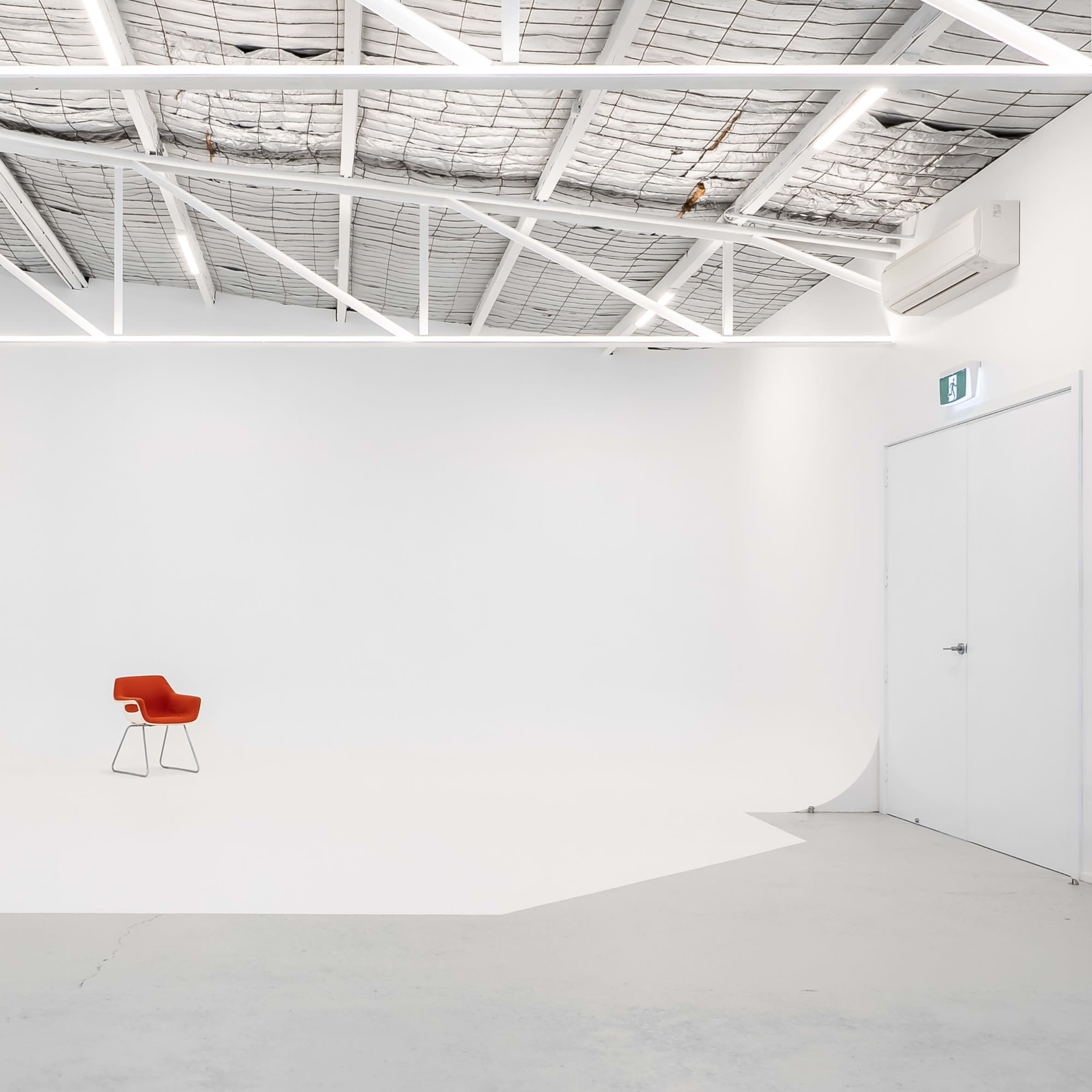 A minimalist studio with a single red chair positioned on a white backdrop, illuminated by overhead lights.