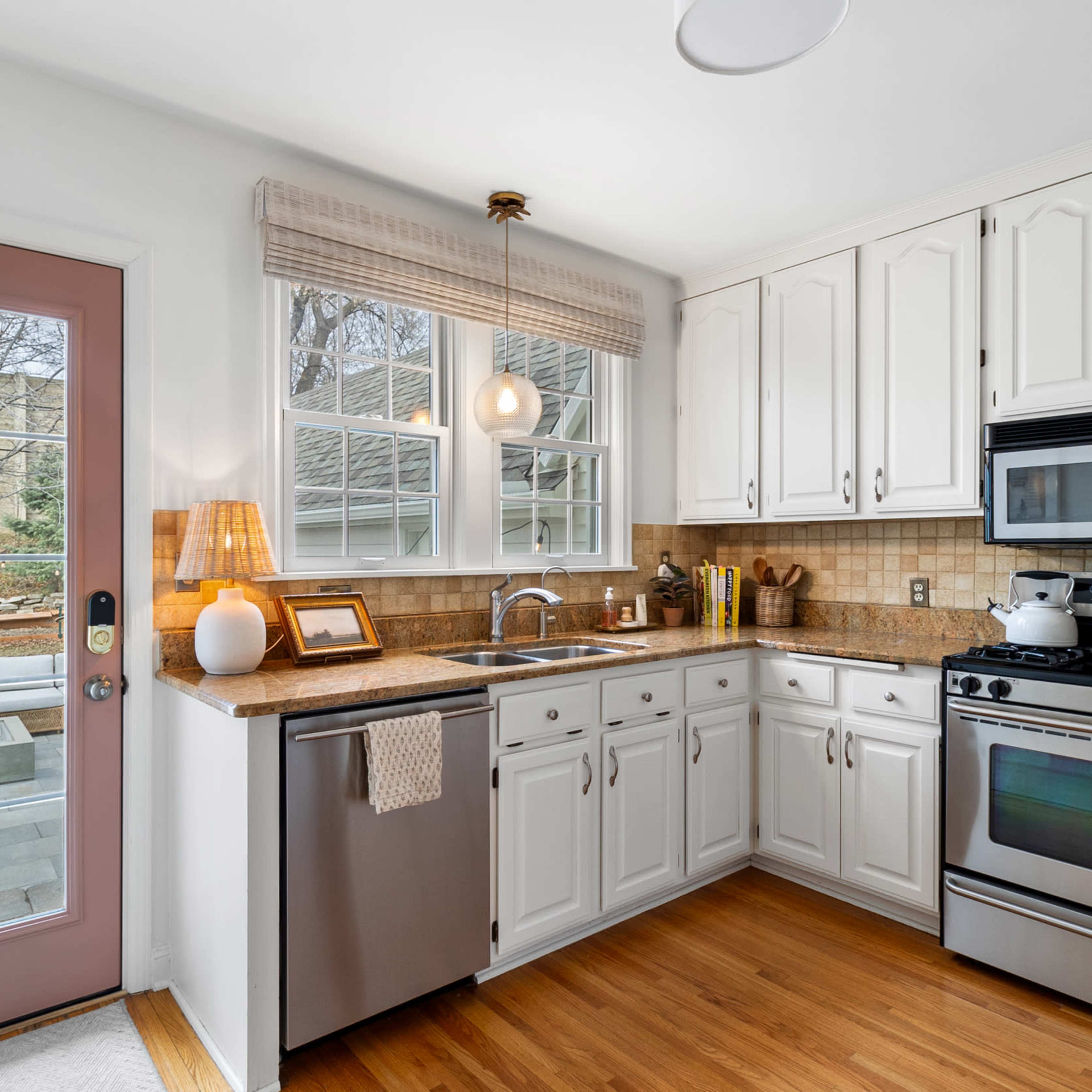 A kitchen with white cabinets, a stainless steel refrigerator, and a dining area visible through a glass door.