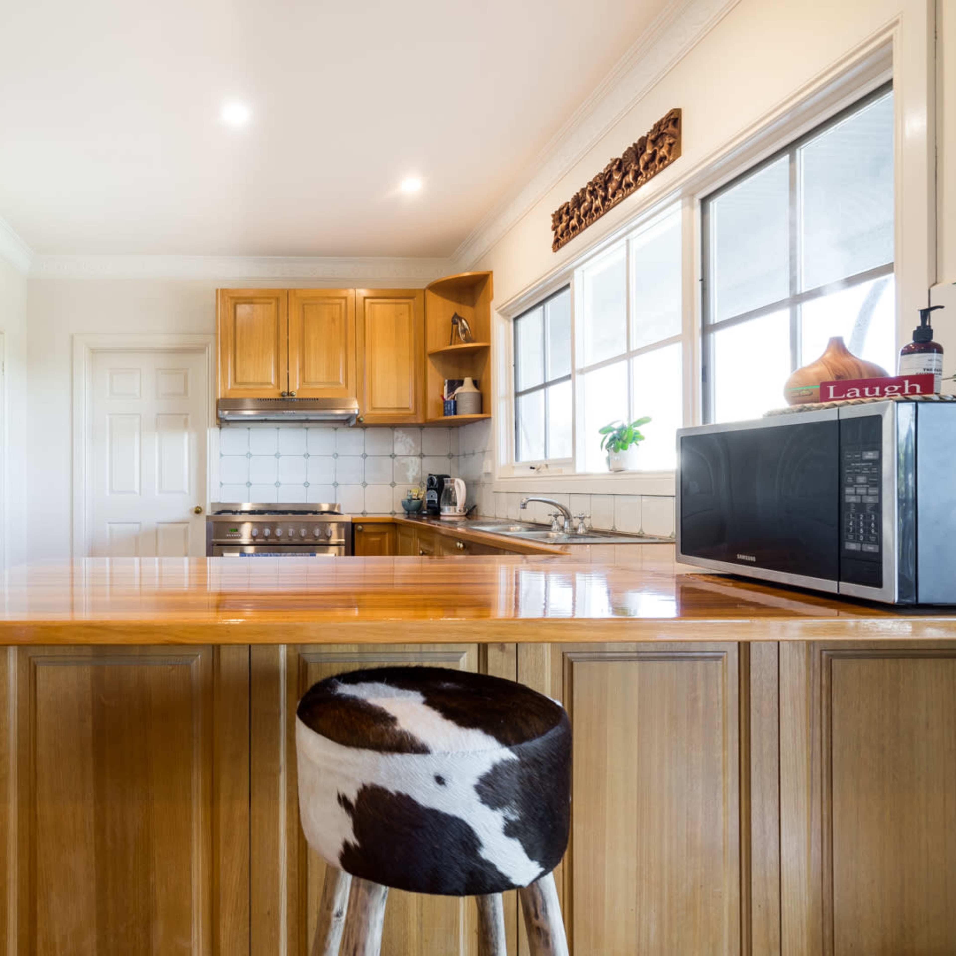 A kitchen features wooden cabinetry, stainless steel appliances, and a counter with a cowhide-styled stool.