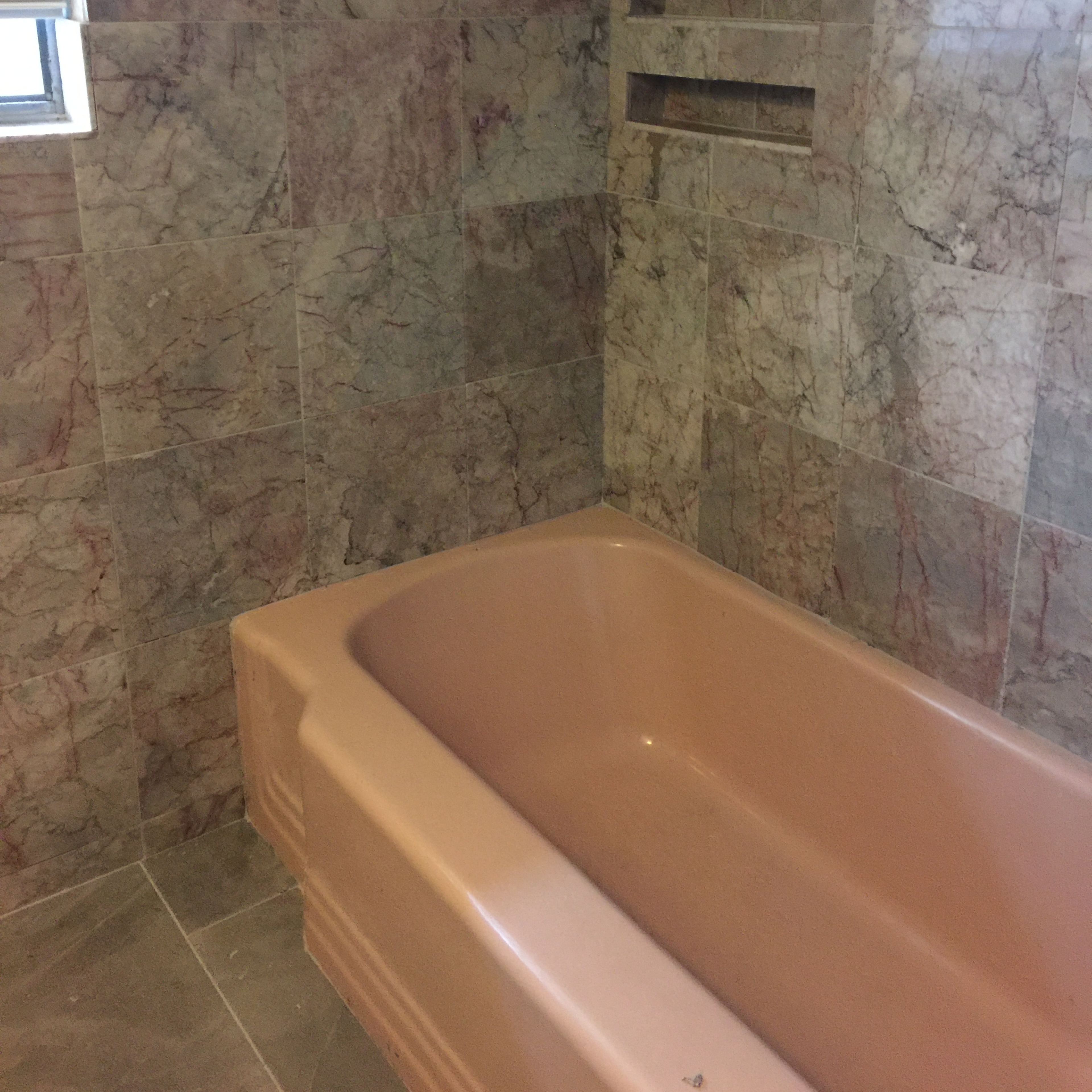 A bathroom with pink marble walls and a beige bathtub.