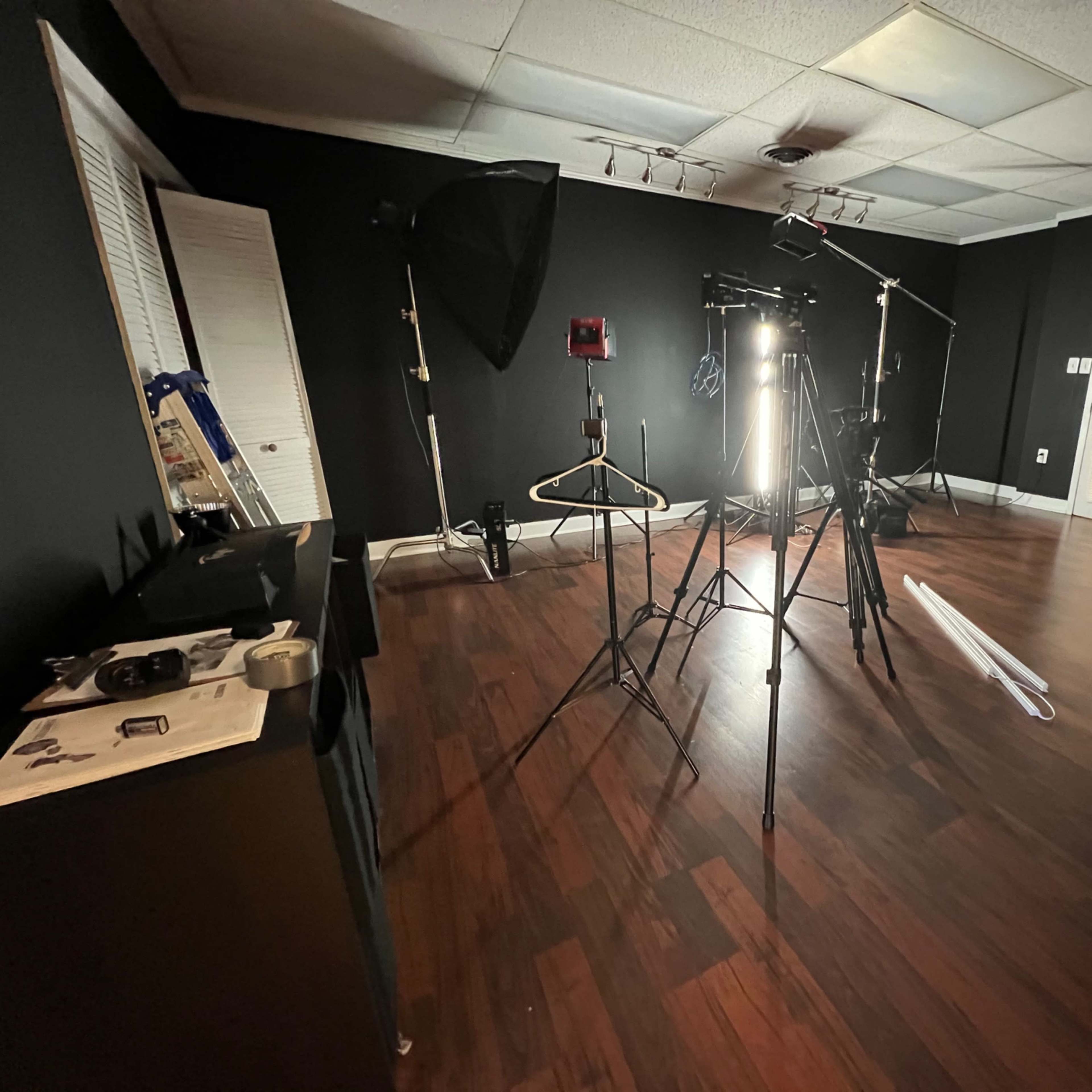 An empty studio space with wooden flooring, equipped with photography lighting and tripods against black walls.
