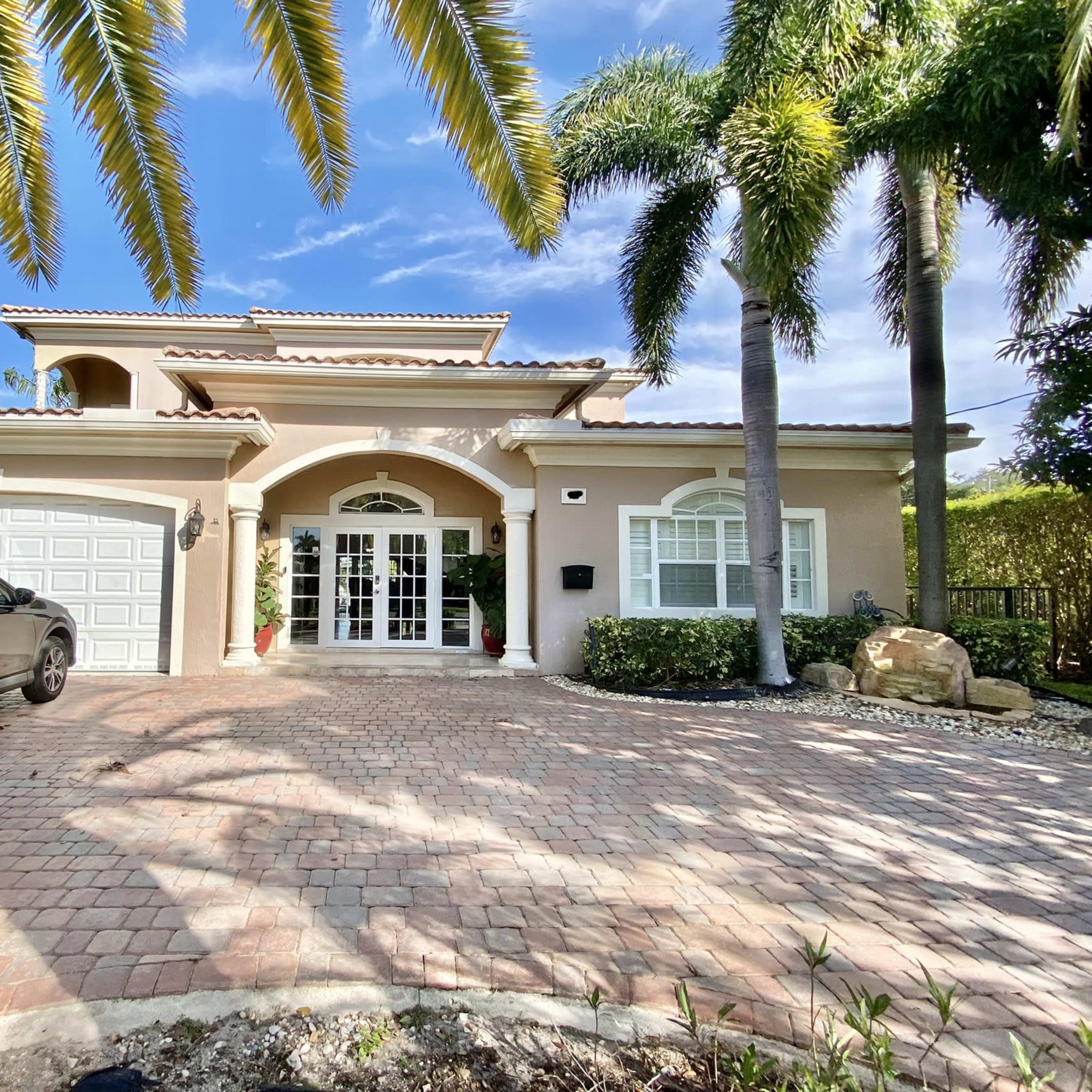 A two-story house with a tiled roof, a brick driveway, and palm trees in the front yard.
