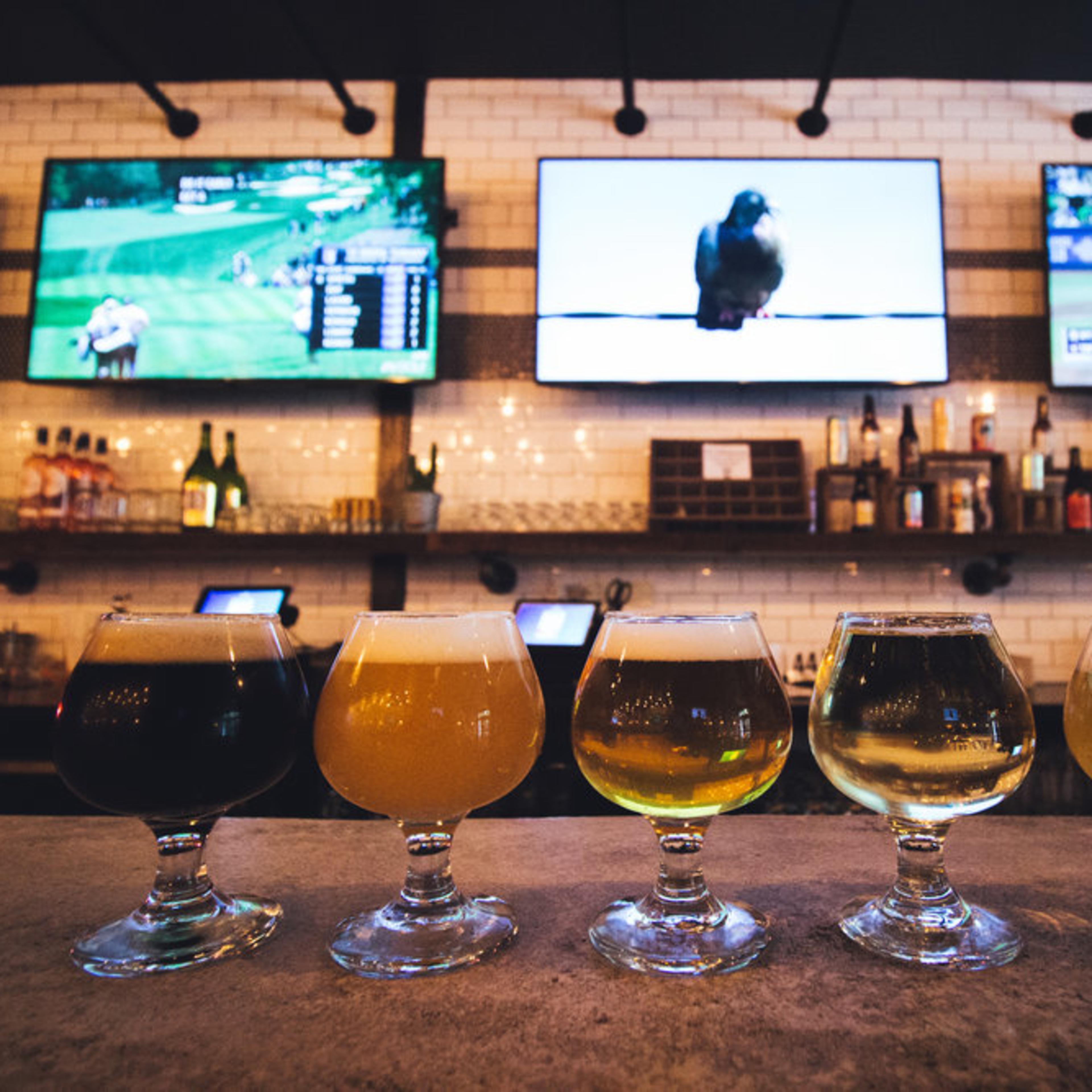 A bar with a concrete countertop, several bar stools, and multiple television screens displaying various sports events.